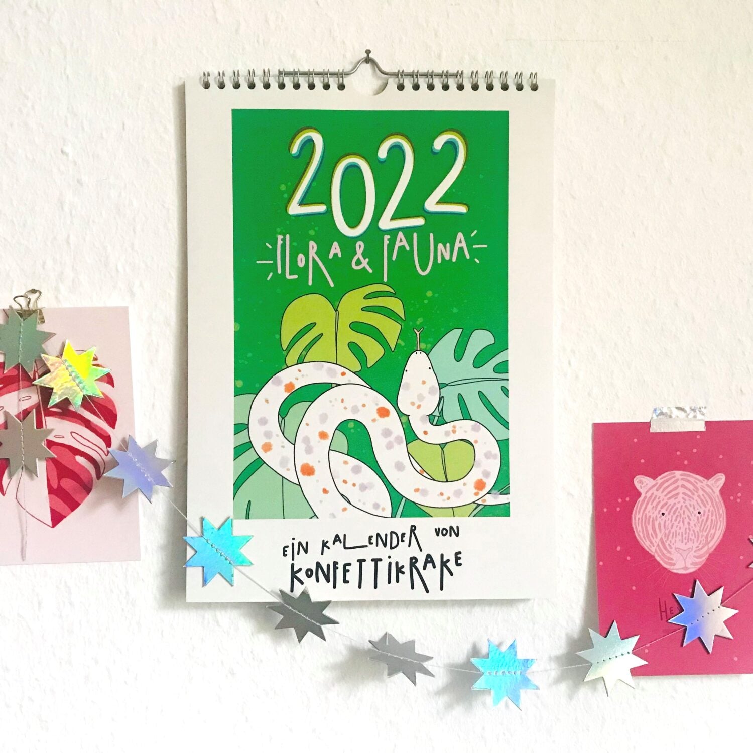 Ein Kalender mit einer Schlange und Pflanzen auf grünem Hintergrund, umgeben von bunten Sternendekorationen.