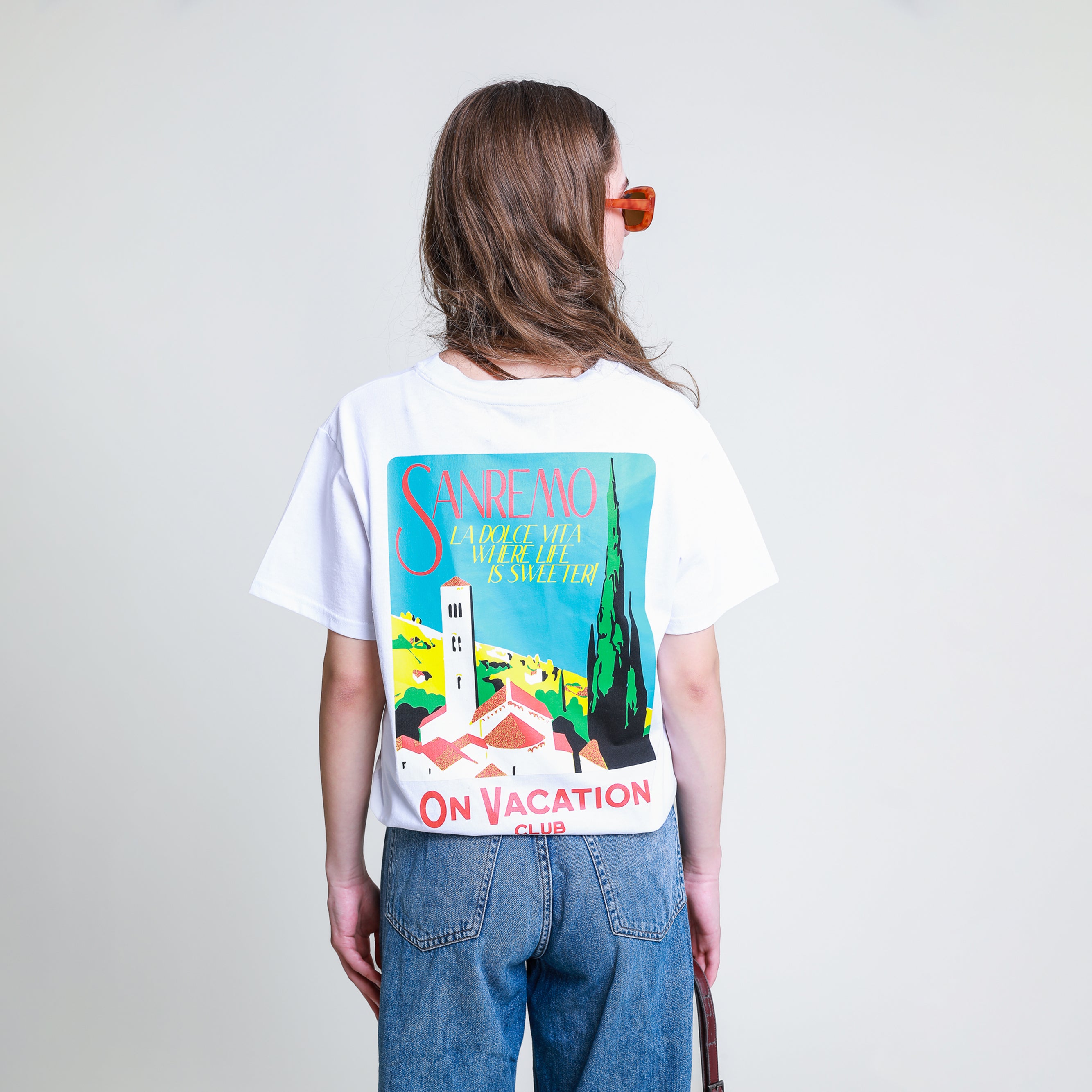 Person mit langen Haaren trägt ein weißes T-Shirt mit einem Sanremo-Urlaubsmotiv auf der Rückseite.