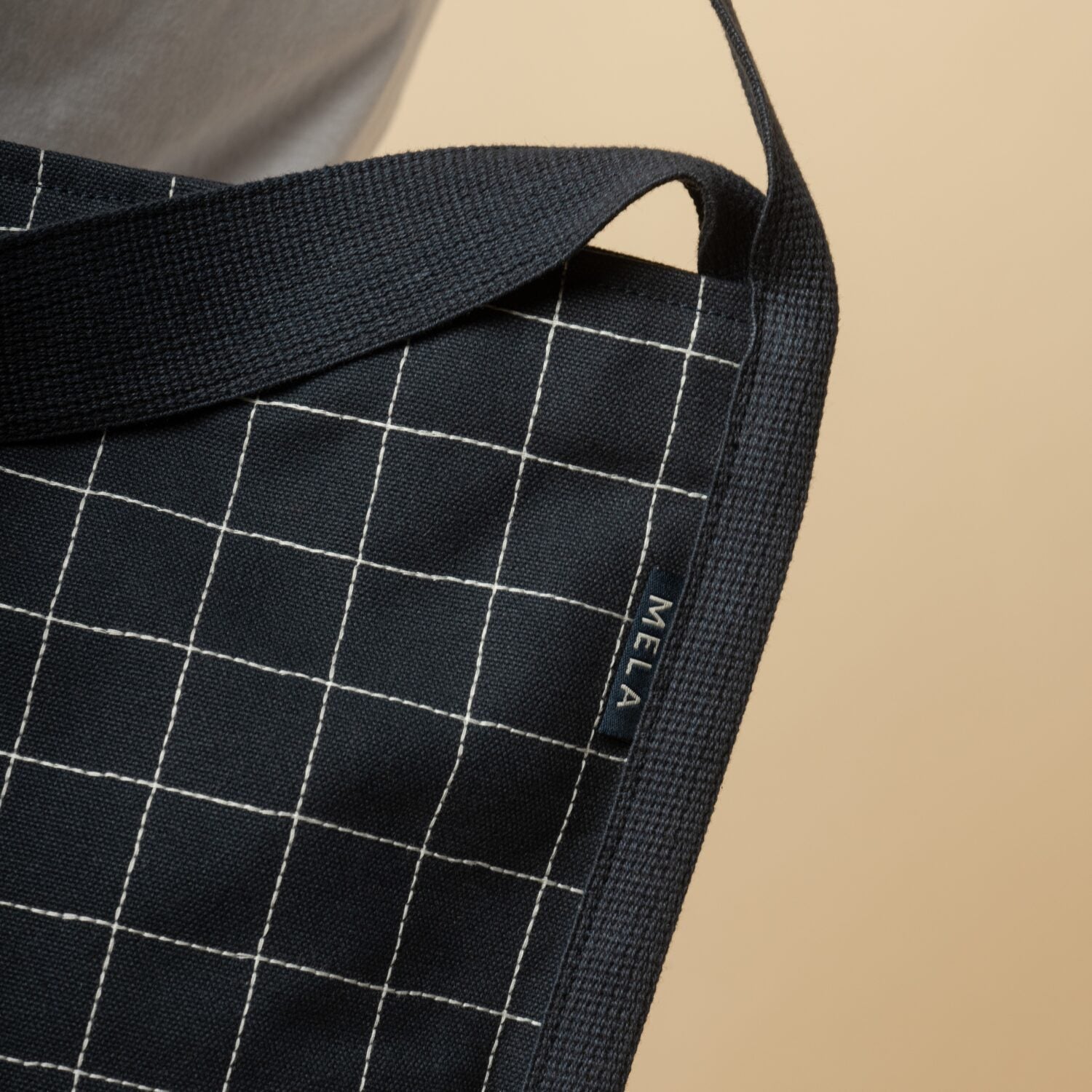 Nahaufnahme einer schwarzen Stofftasche mit weißem Karomuster und einem Etikett, auf dem "MELA" steht.
