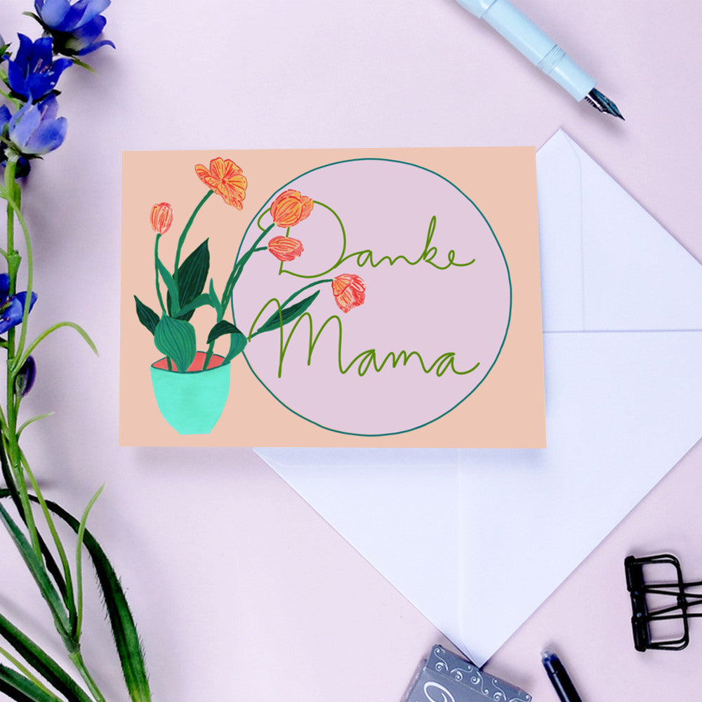 Karte mit Blumenmotiv und der Aufschrift "Danke Mama" liegt auf einem Umschlag, umgeben von Blumen und einem Stift.