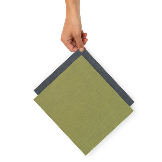 Eine Hand hält zwei überlappende, quadratische Stoffmuster in Olivgrün und Dunkelgrau.