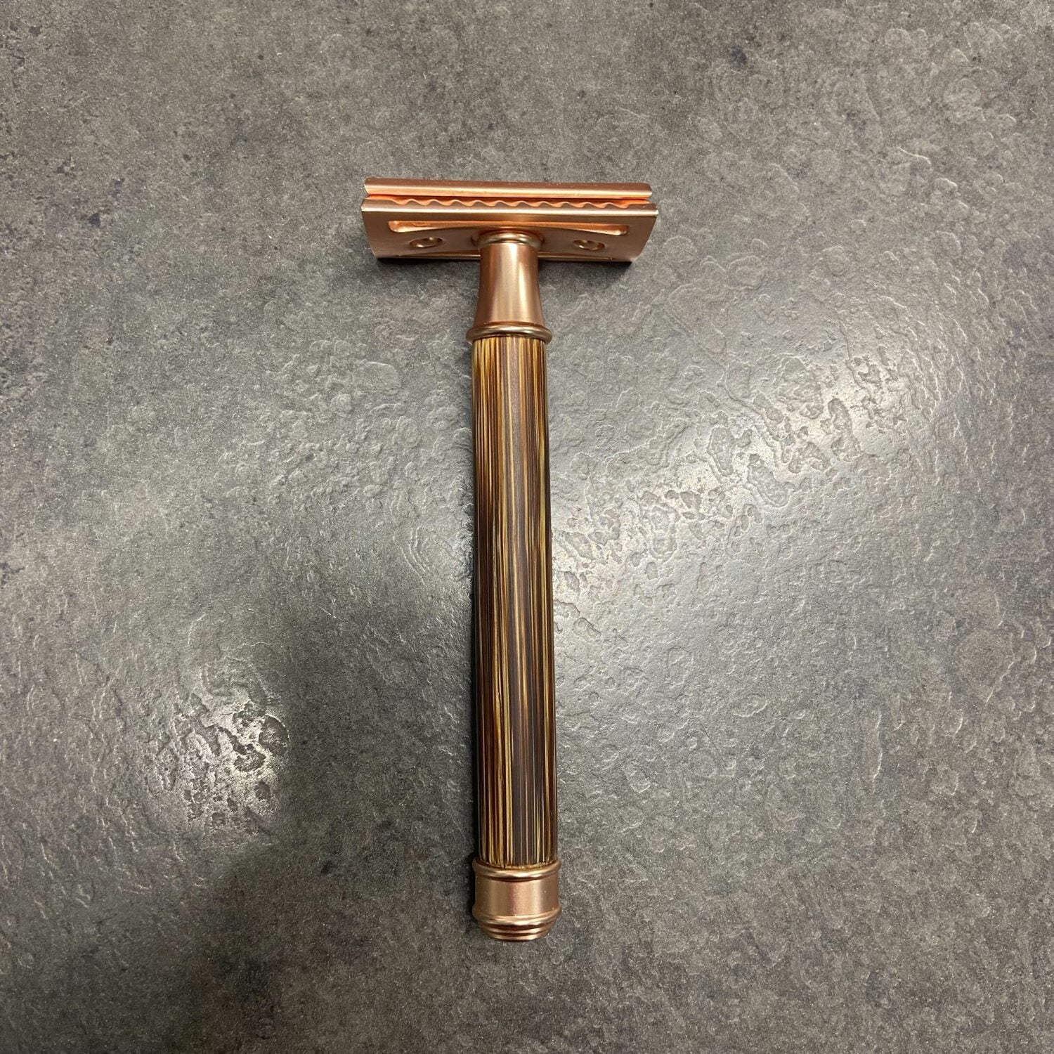 Kupferfarbener Rasierhobel auf einem dunklen, strukturierten Untergrund.