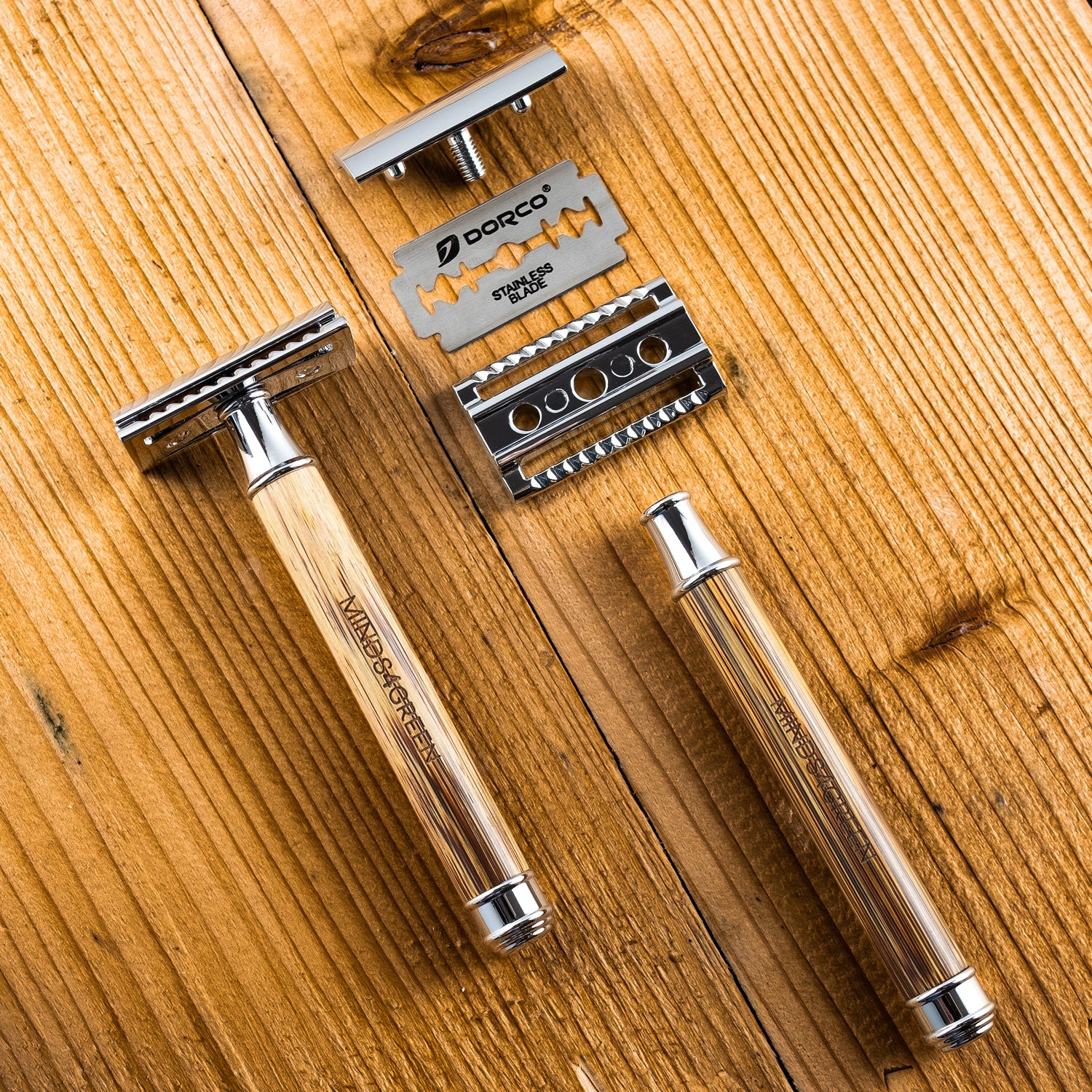 Rasierapparat mit Holzgriff und Ersatzklinge auf einem Holztisch liegend, mit separaten Metallteilen.