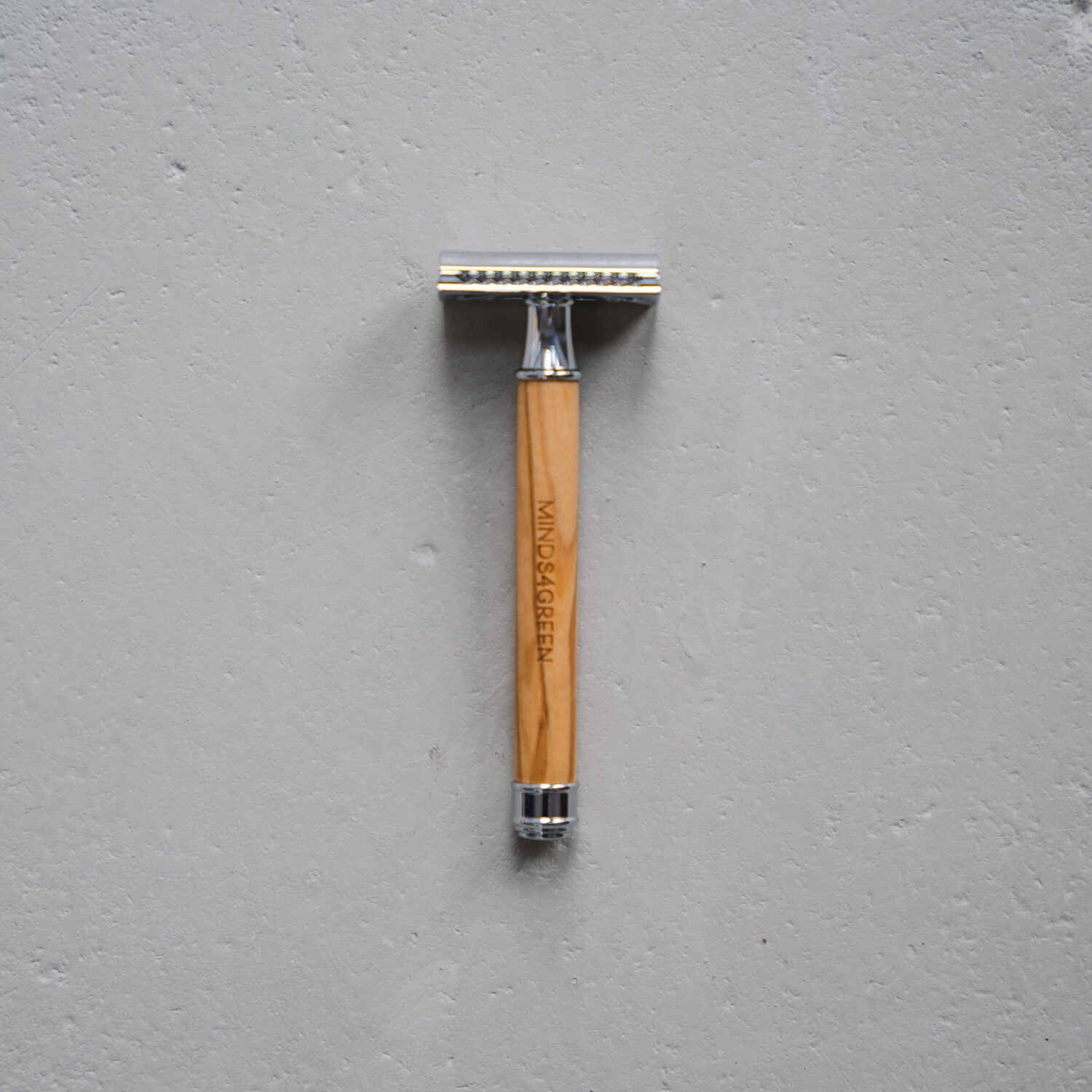 Ein Rasierhobel mit einem Holzgriff, auf dem "MIND S4GREEN" eingraviert ist, liegt auf einer grauen Oberfläche.
