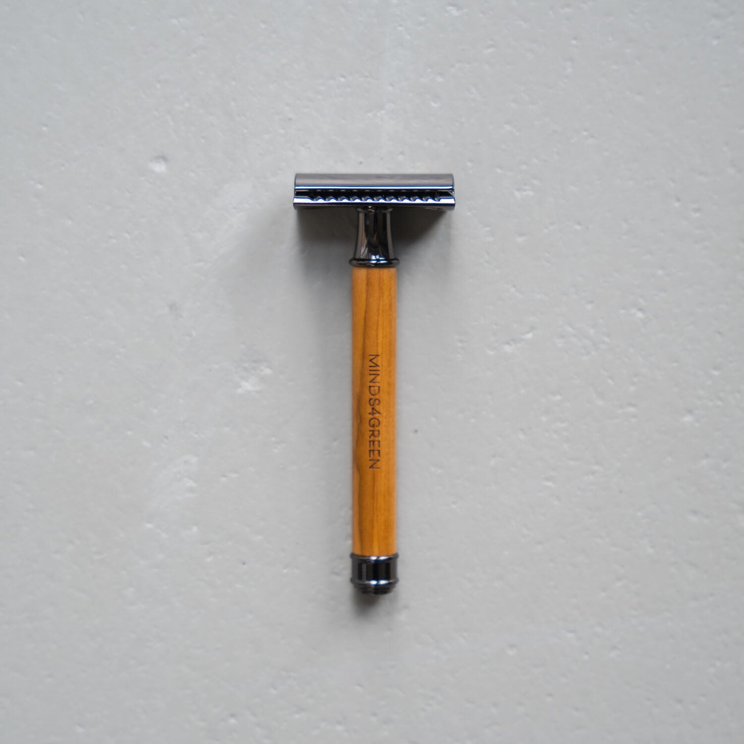 Rasierhobel mit Holzgriff und silbernem Kopf liegt auf einer grauen Oberfläche.