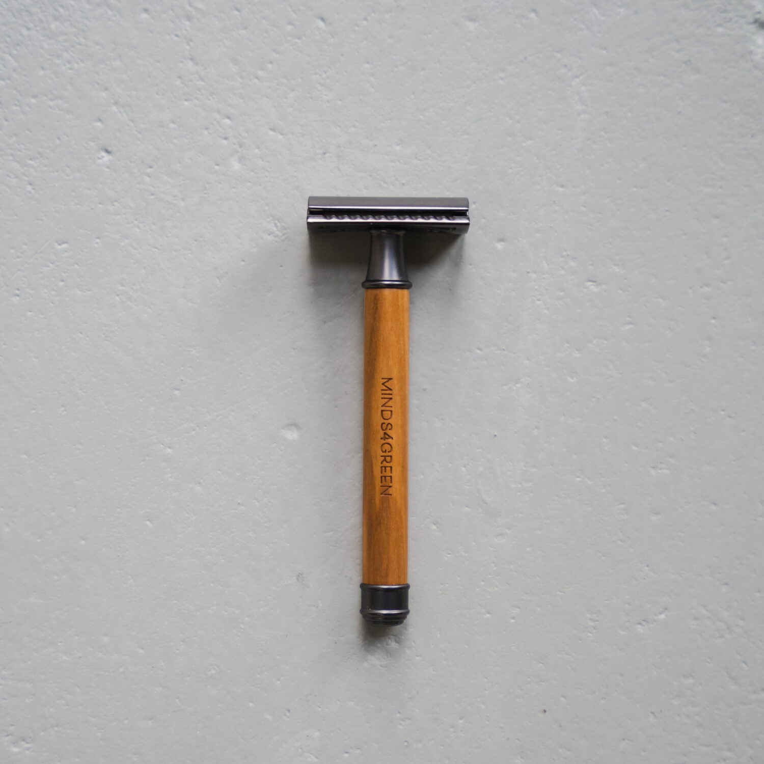Holzrasierer mit Metalleinfassung auf grauem Hintergrund, mit "MINDS4GREEN" auf dem Griff eingraviert.