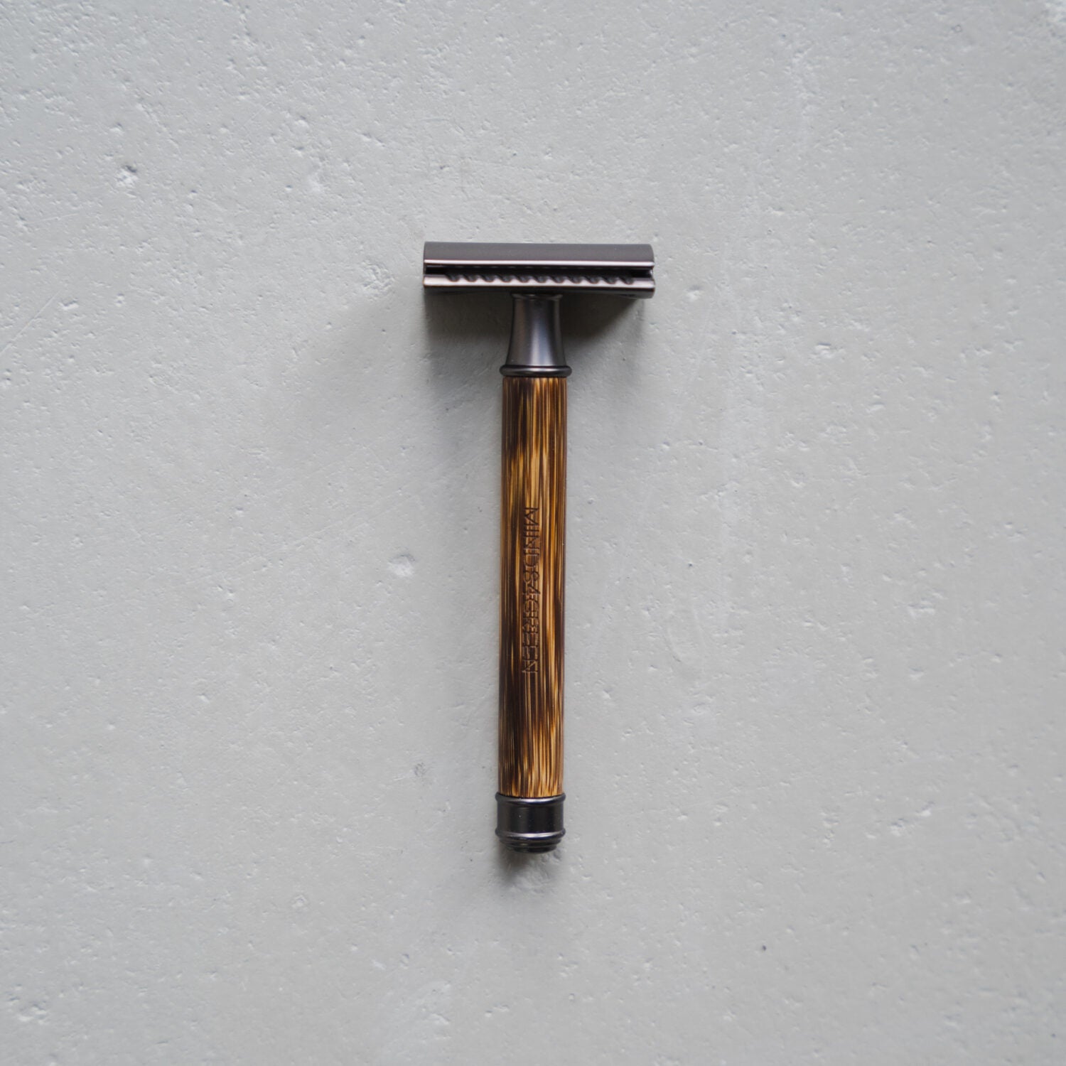 Ein klassischer Rasierhobel mit braunem Griff liegt auf einer grauen Oberfläche.