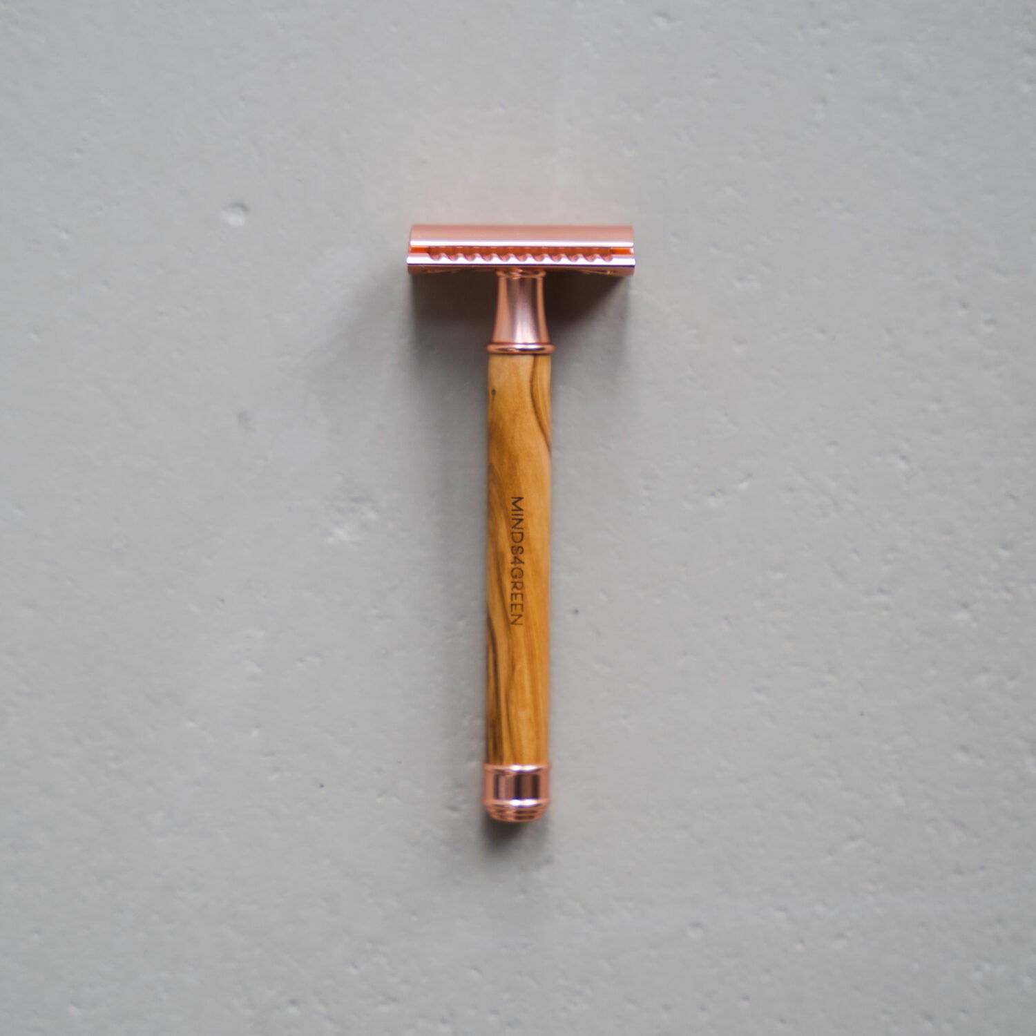 Rasierhobel mit Holzgriff und roségoldener Metallklinge auf grauem Hintergrund.