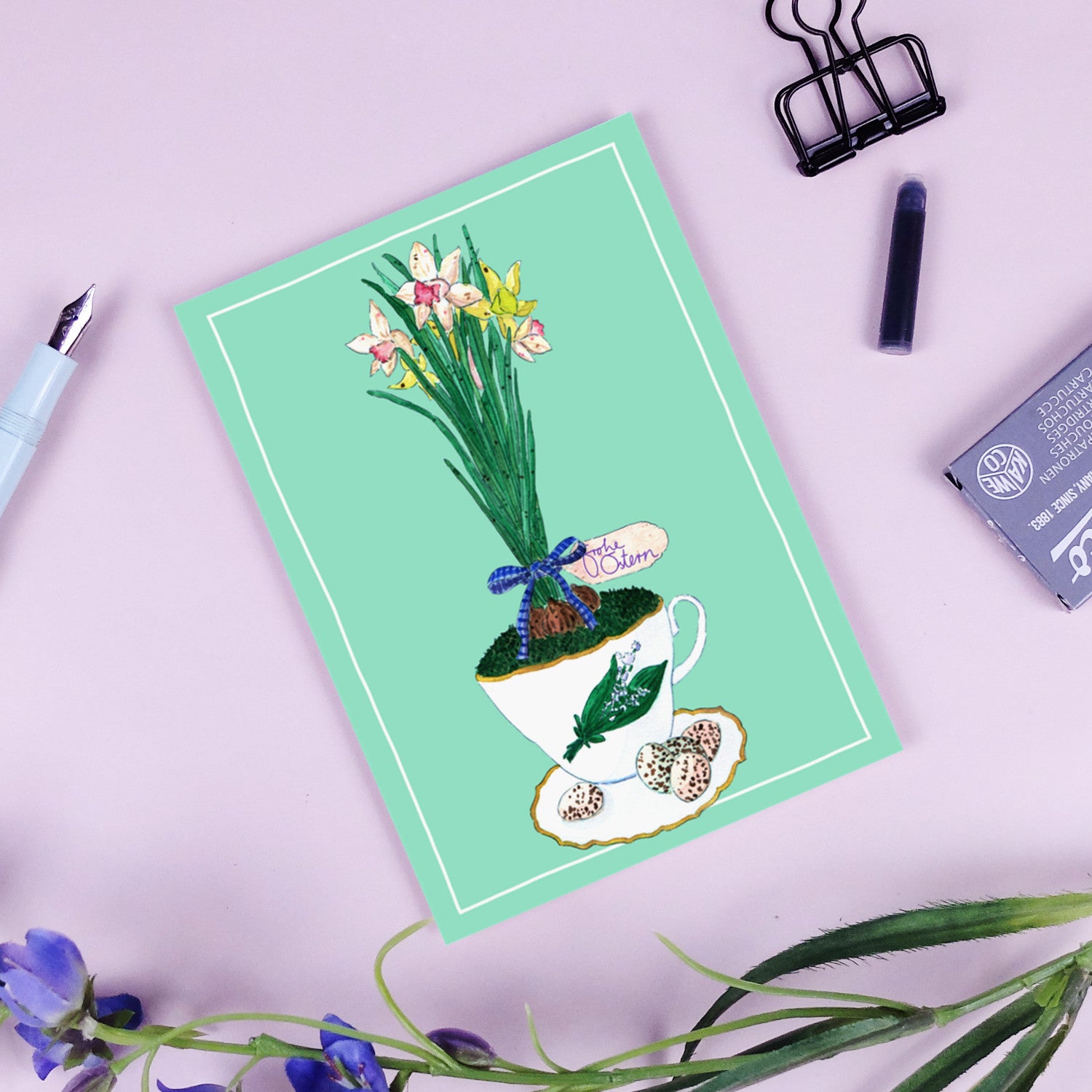 Illustration einer Teetasse mit Blumen, dekoriert mit einem "Frohe Ostern"-Schild, auf grünem Hintergrund.
