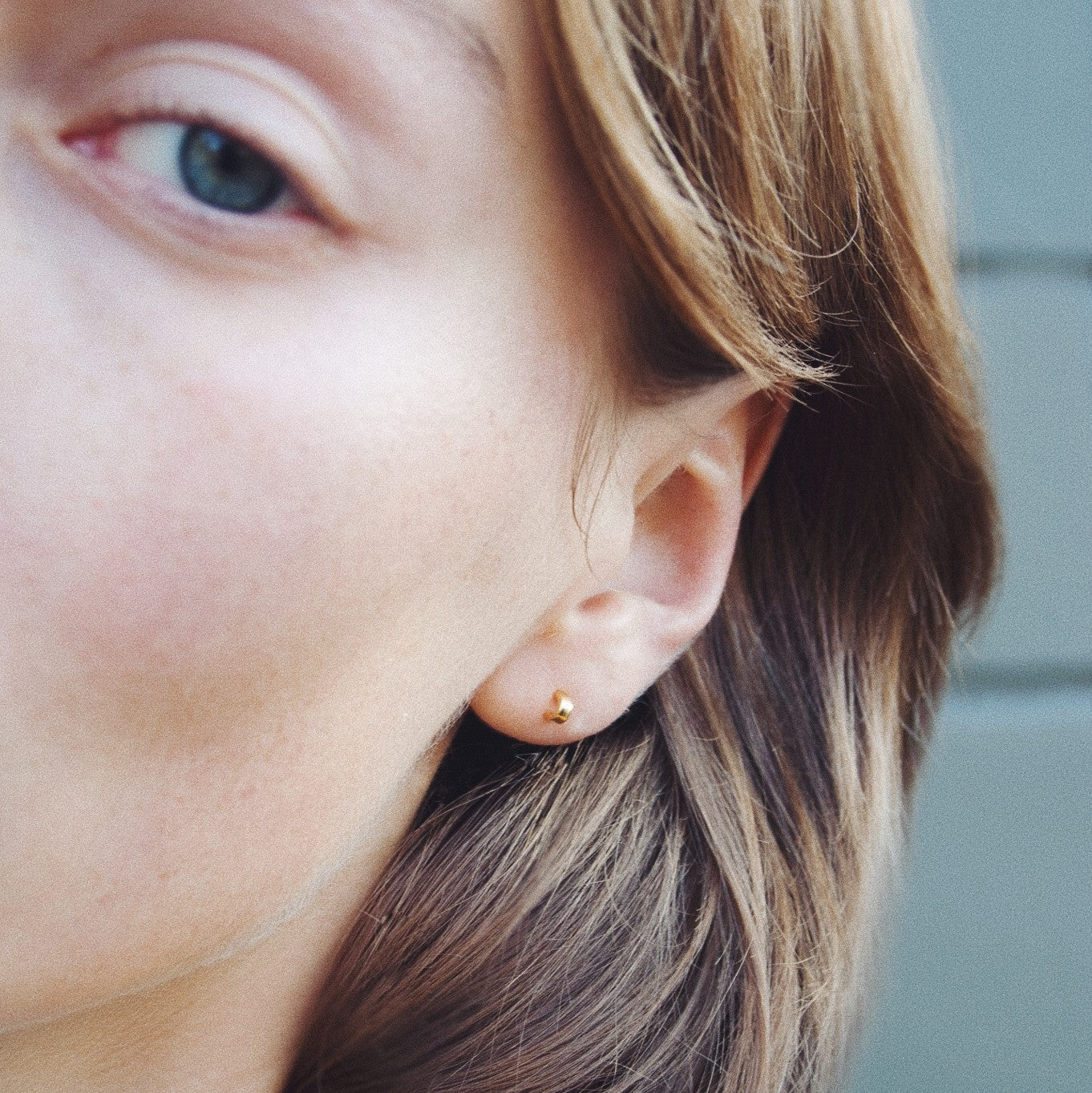 Nahaufnahme eines menschlichen Ohrs mit kurzem Haar, das einen kleinen, runden, goldenen Ohrring trägt.