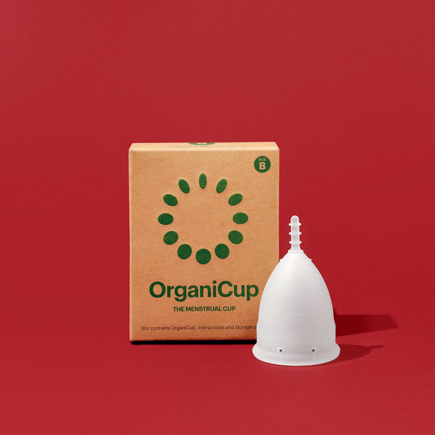 Verpackung und Menstruationstasse der Marke OrganiCup vor rotem Hintergrund.