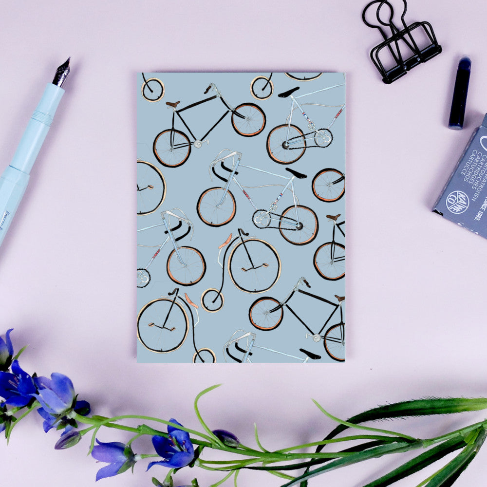 Papier auf einem Tisch mit Fahrradmustern, umgeben von Blumen, einem Füllfederhalter und einem schwarzen Clip.