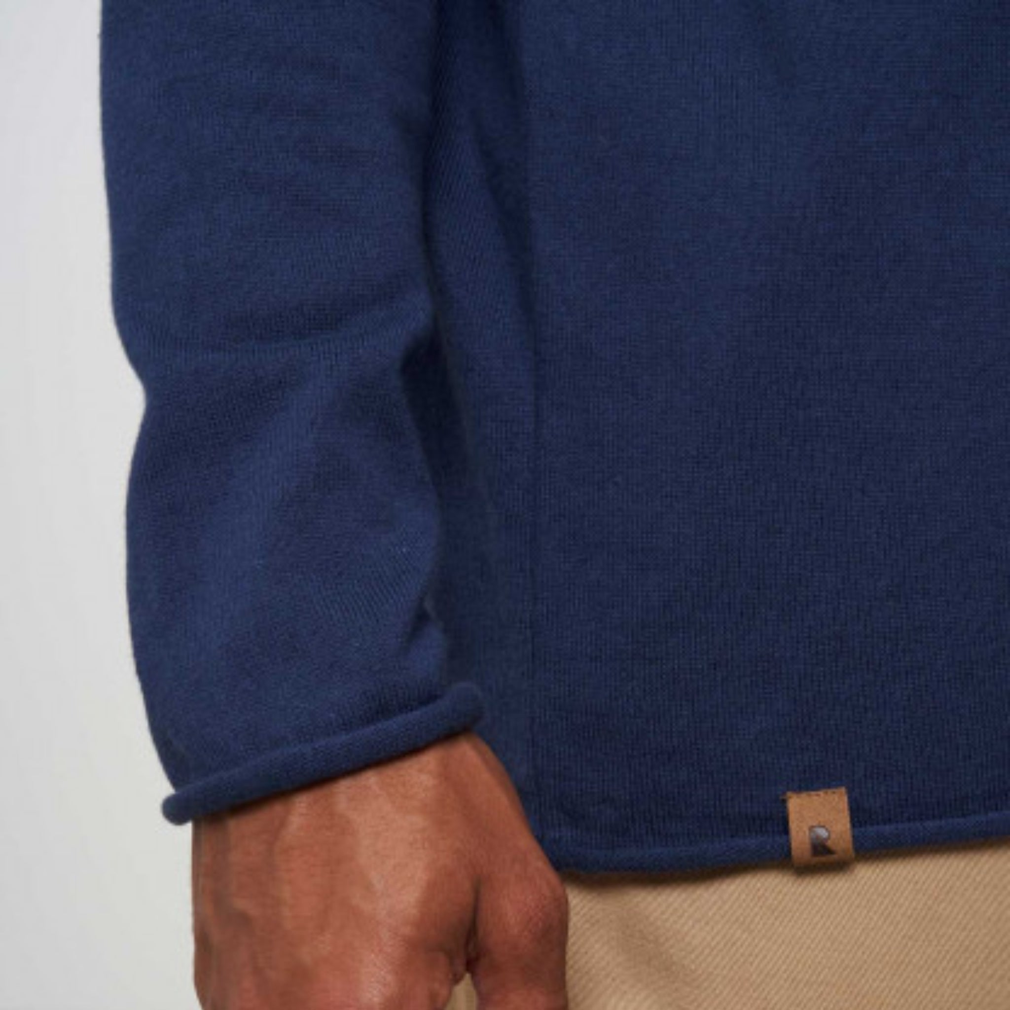 Person in navy sweater and beige pants, with visible hand near the side seam of the garment.