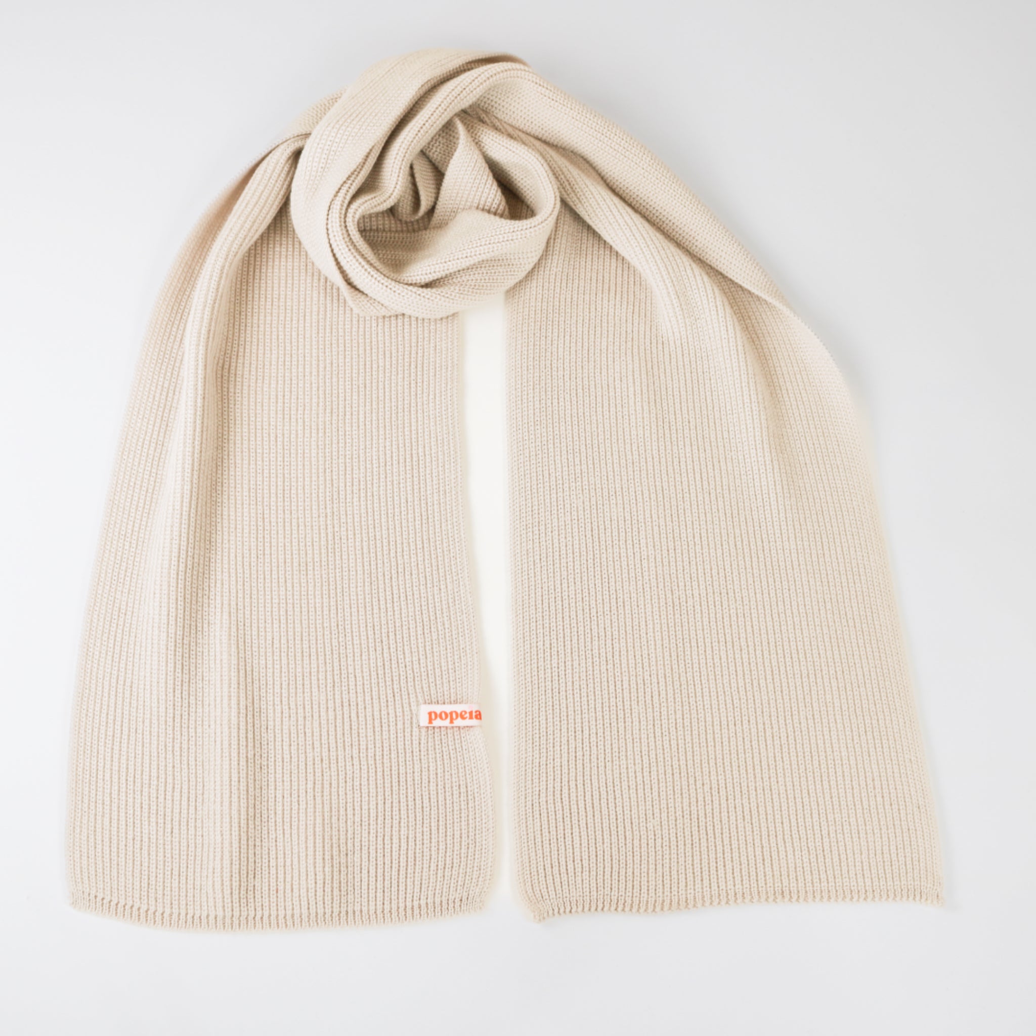 Beiger Strickschal mit einer roten Markierung, auf einer weißen Oberfläche drapiert.