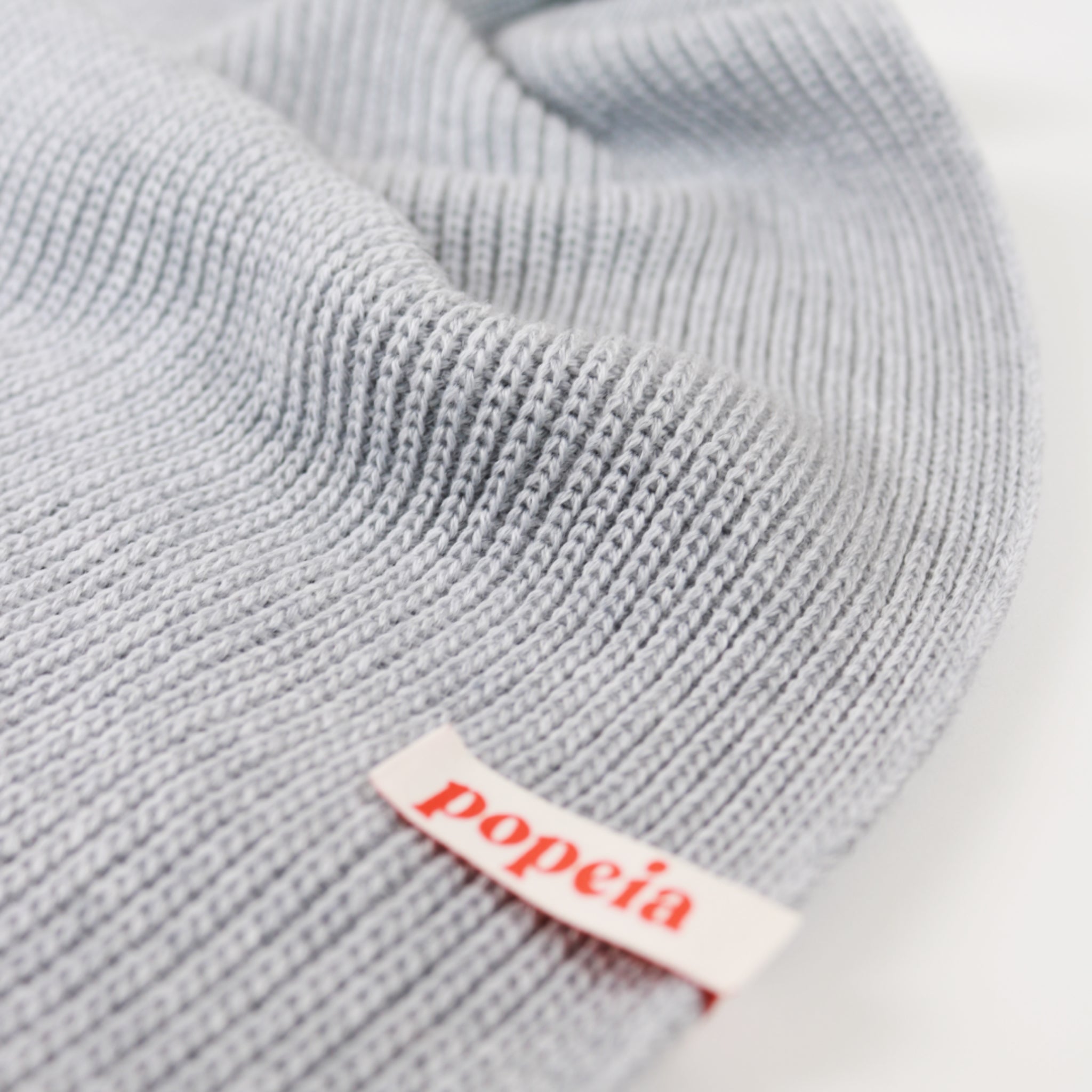 Graue Strickmütze mit einem Etikett, auf dem "popeia" in roten Buchstaben steht.