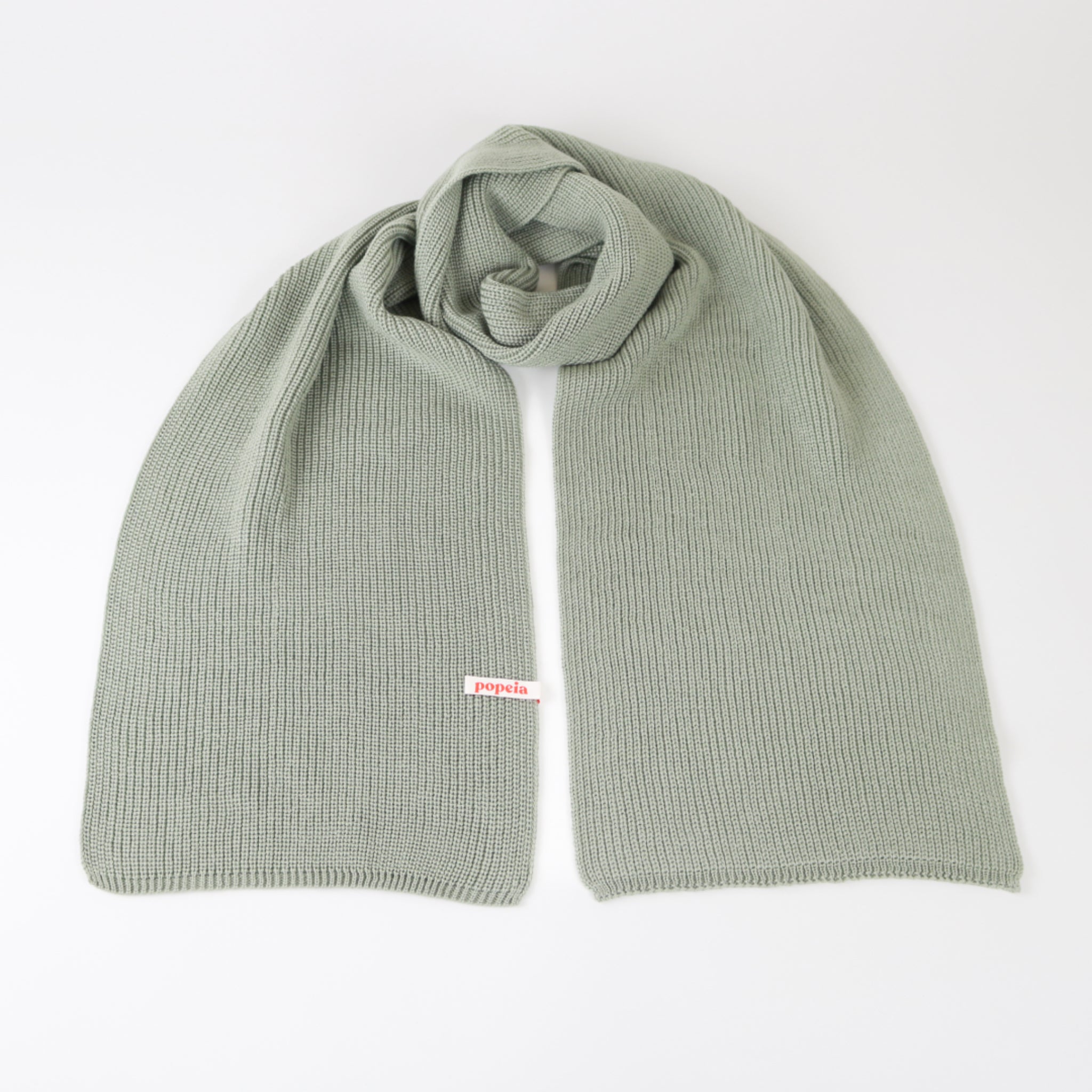 Hellgrauer Strickschal aus Wolle, ordentlich gefaltet auf einer weißen Oberfläche.