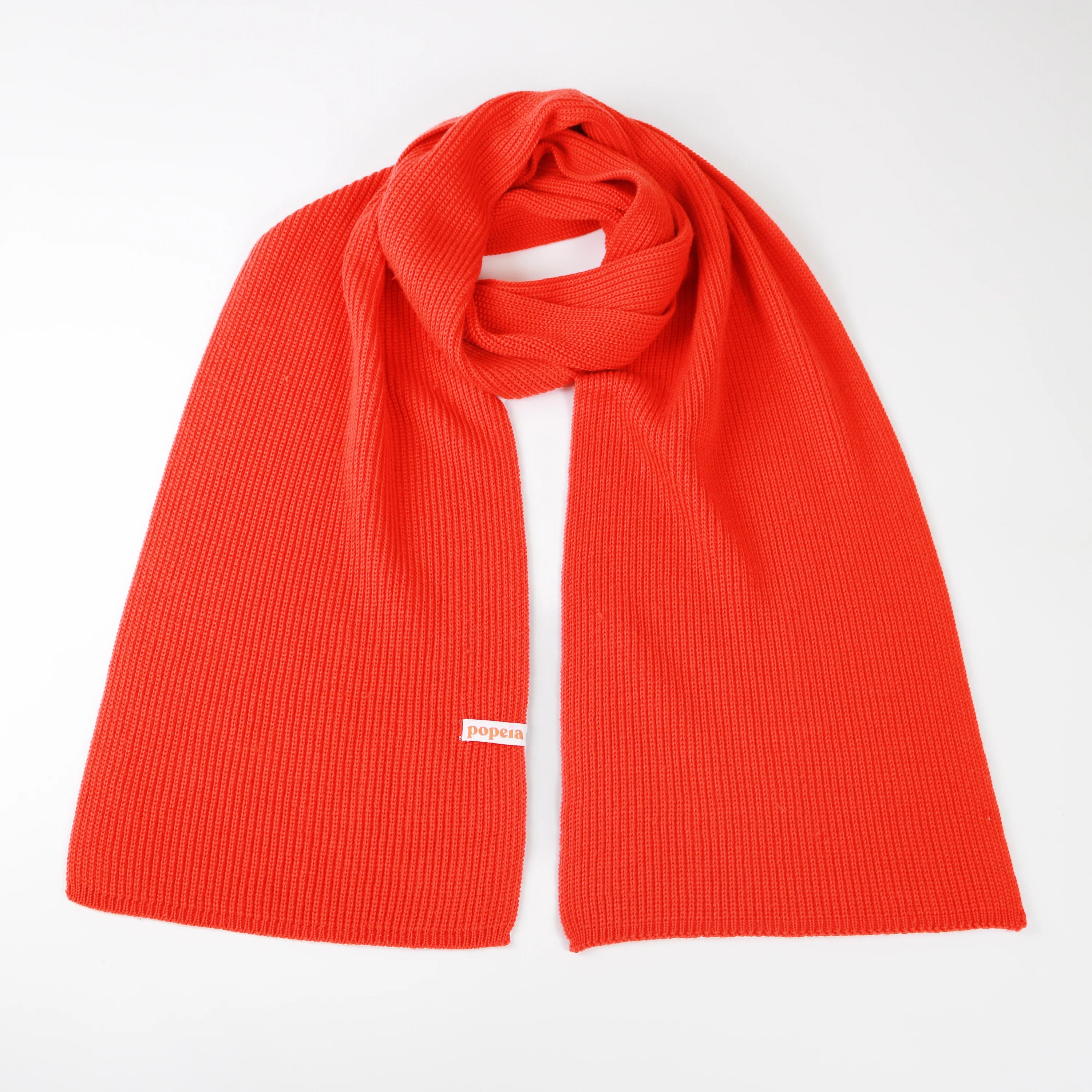 Roter Strickschal mit Etikett auf weißem Hintergrund drapiert.