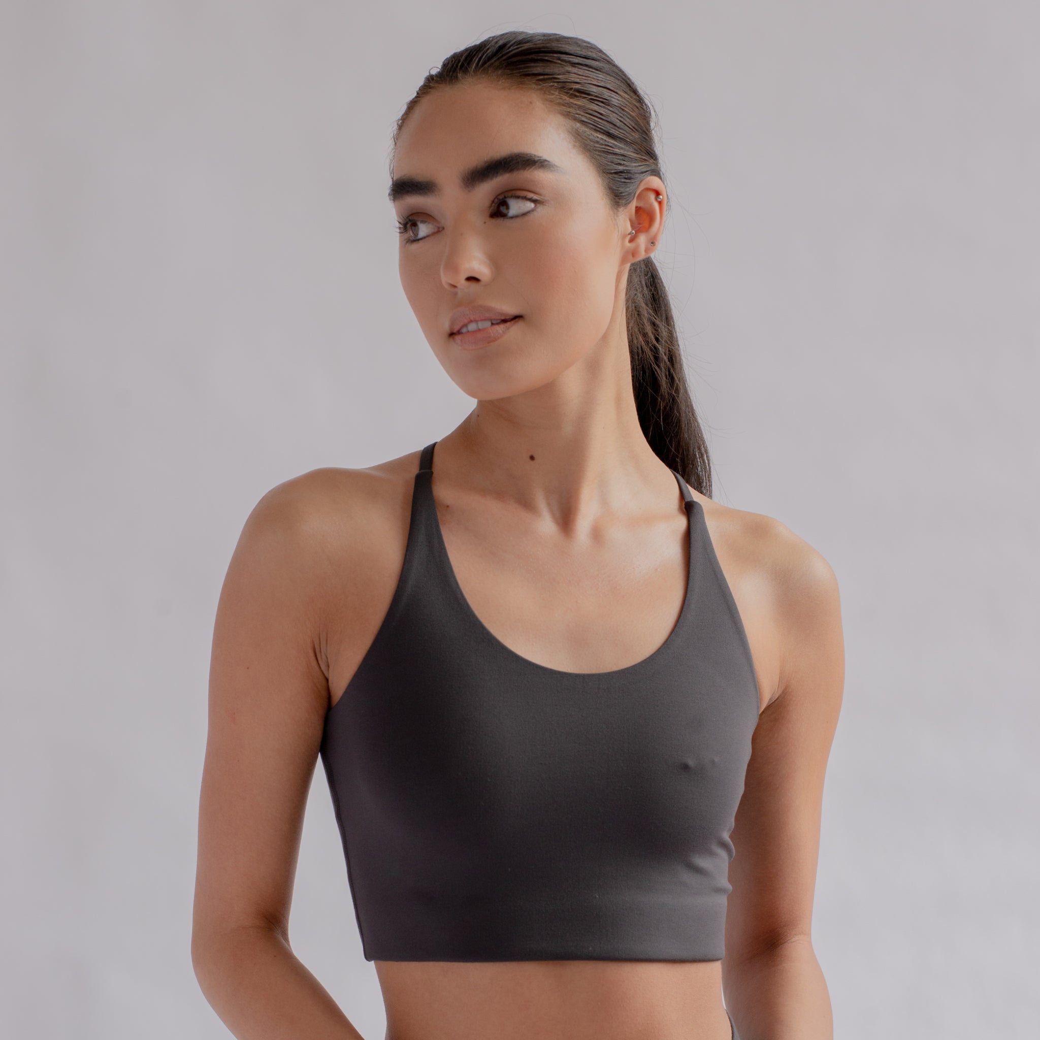 Frau in einem grauen Sport-BH schaut nach links vor einem neutralen Hintergrund.