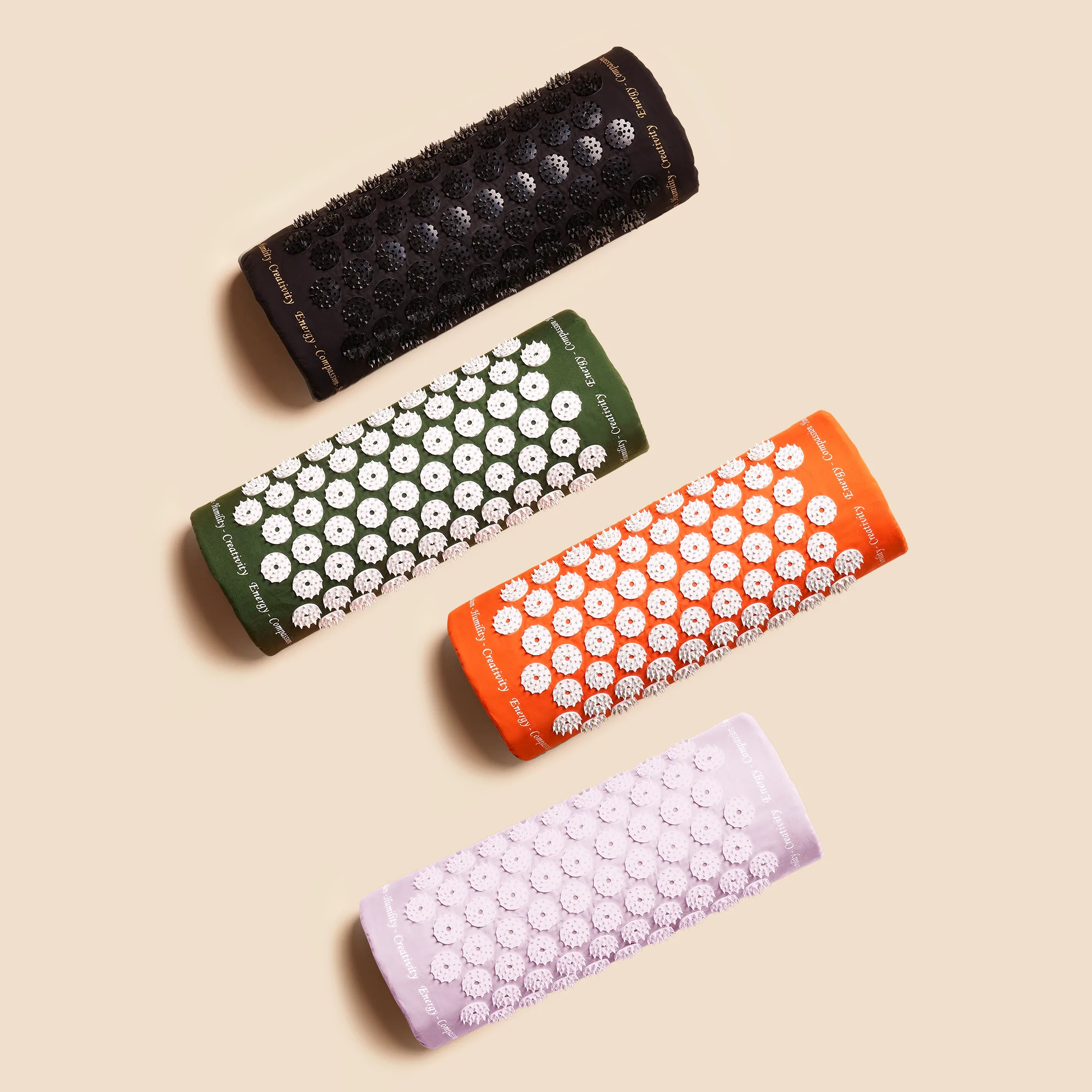 Vier Akupressur-Matten in Schwarz, Grün, Orange und Lila auf beigem Hintergrund.