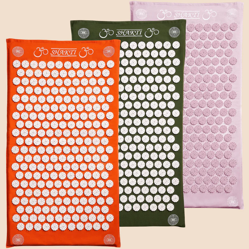 Drei Akupressurmatten in Orange, Grün und Rosa mit kreisförmigen weißen Mustern auf beigem Hintergrund.