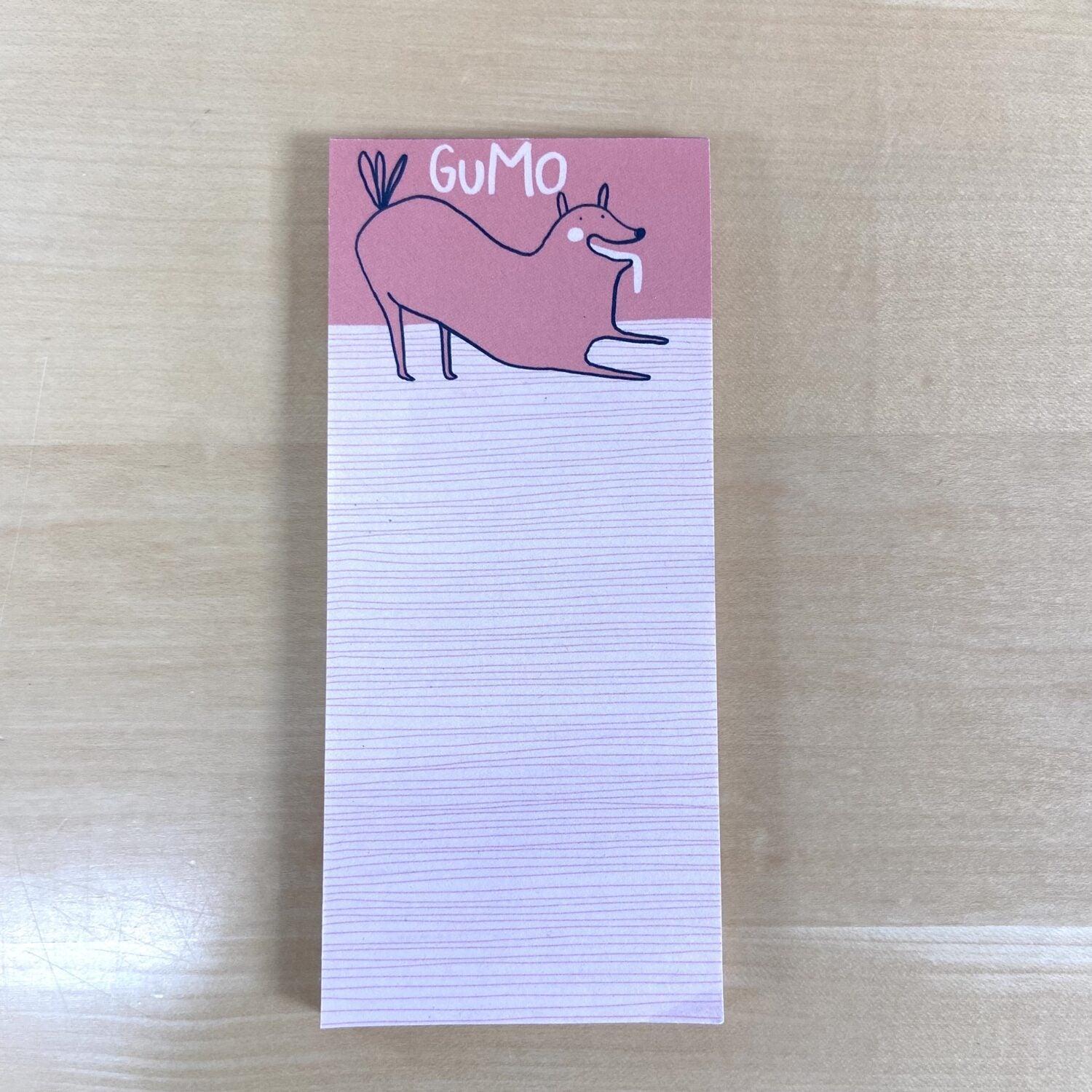 Ein Notizblock mit einem gezeichneten Hund oben, der "GuMo" sagt, liegt auf einem Holztisch.