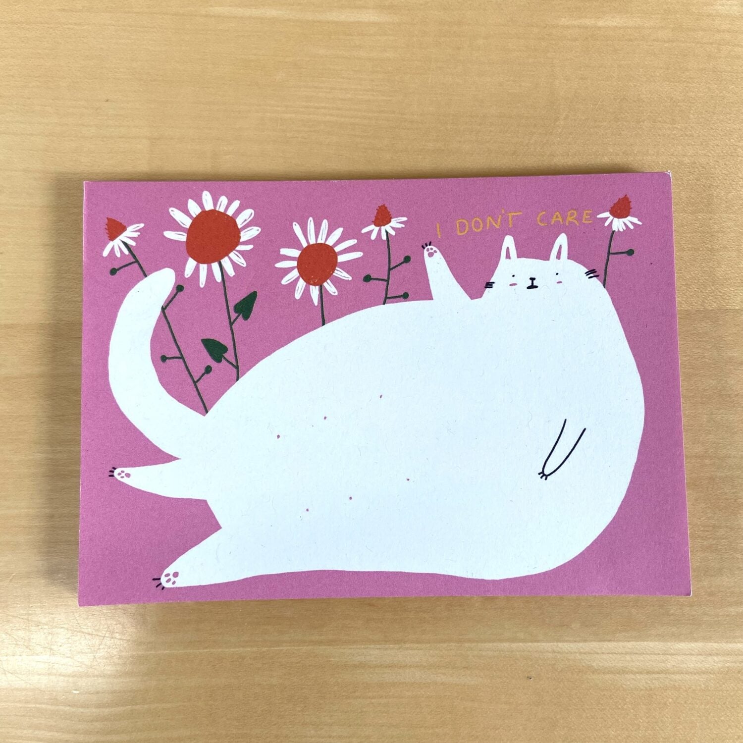 Illustration einer weißen Katze, die auf einem rosa Hintergrund mit Blumen liegt; daneben steht "I don't care".