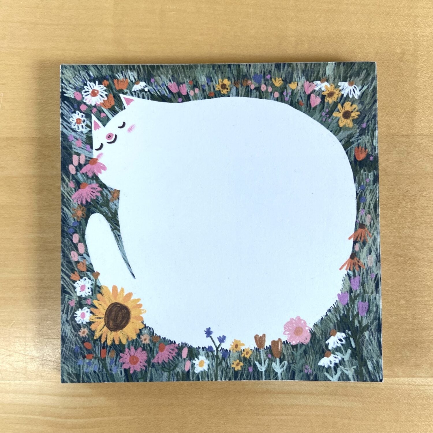 Illustration einer großen weißen Katze umgeben von einem bunten Blumenkranz auf einem Holzuntergrund.