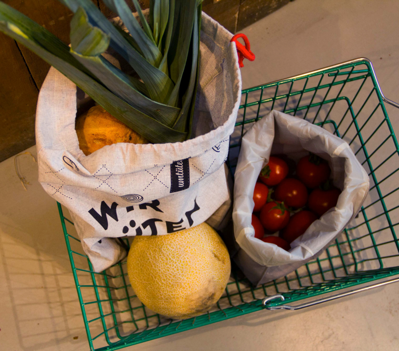 Ein Einkaufswagen mit wiederverwendbaren Beuteln gefüllt mit Lauch, Melone und Tomaten.