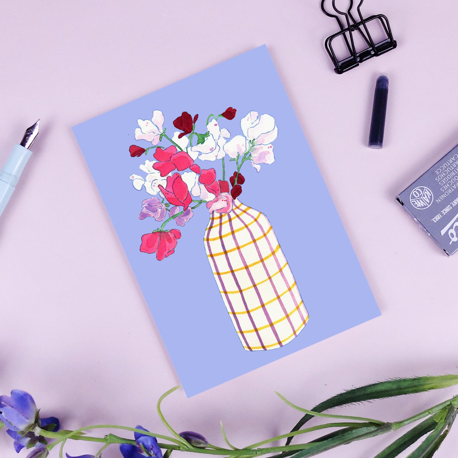 Karte mit Illustration: bunte Blumen in einer karierten Vase auf blauem Hintergrund, daneben ein Füllfederhalter und Büroklammer.