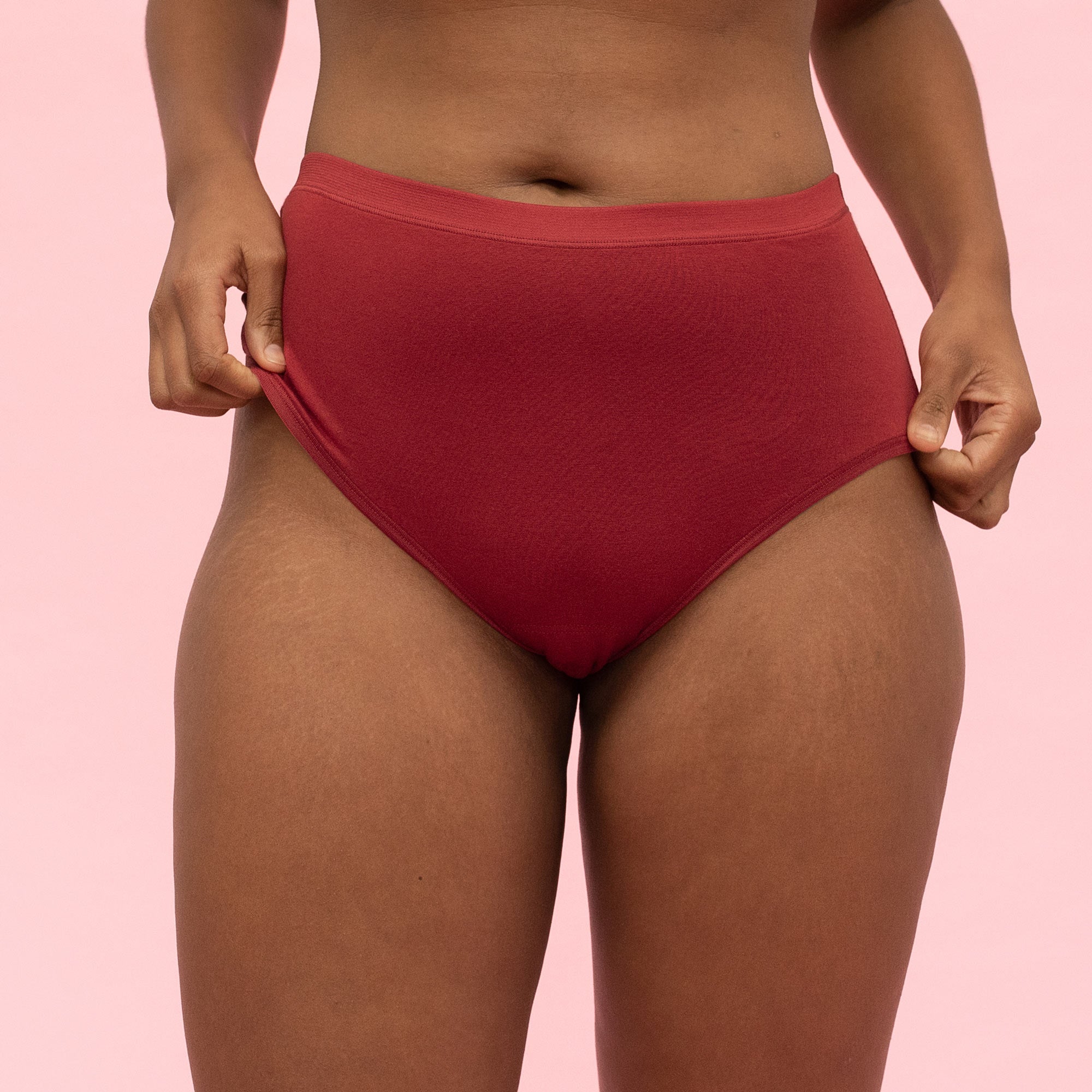 Person in roten Unterhosen vor rosa Hintergrund, Nahaufnahme der Hüfte und Oberschenkel.