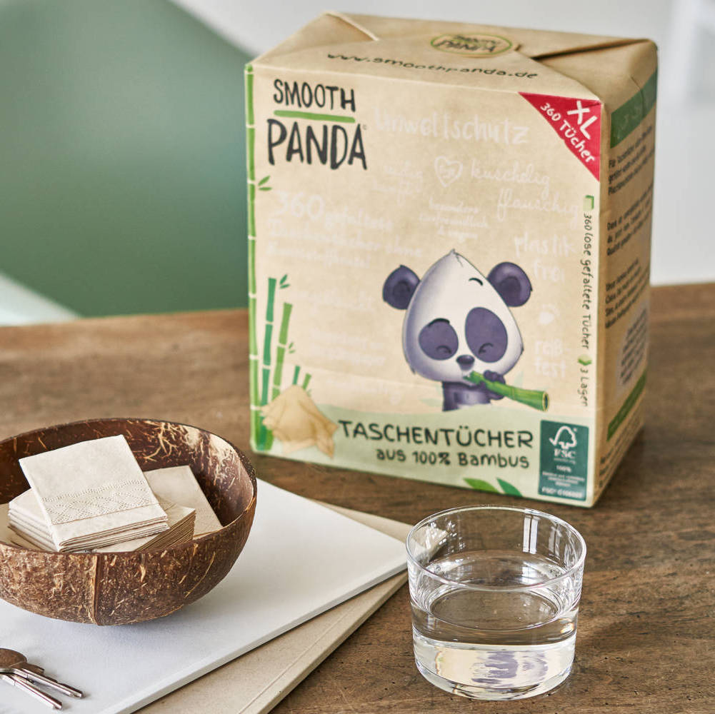 Box mit Smooth Panda Taschentüchern aus Bambus, daneben eine Schale und ein Glas Wasser auf einem Tisch.