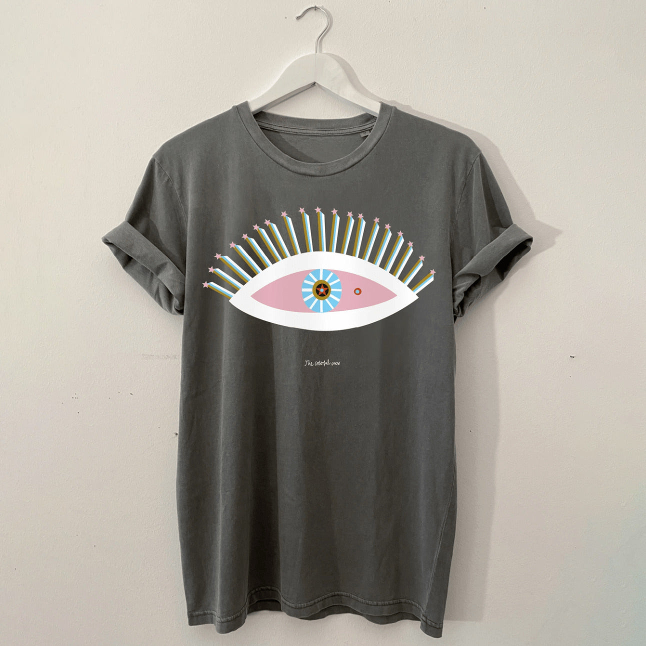 Graues T-Shirt mit großem buntem Augendesign und bunten Wimpern, auf einem weißen Kleiderbügel hängend.
