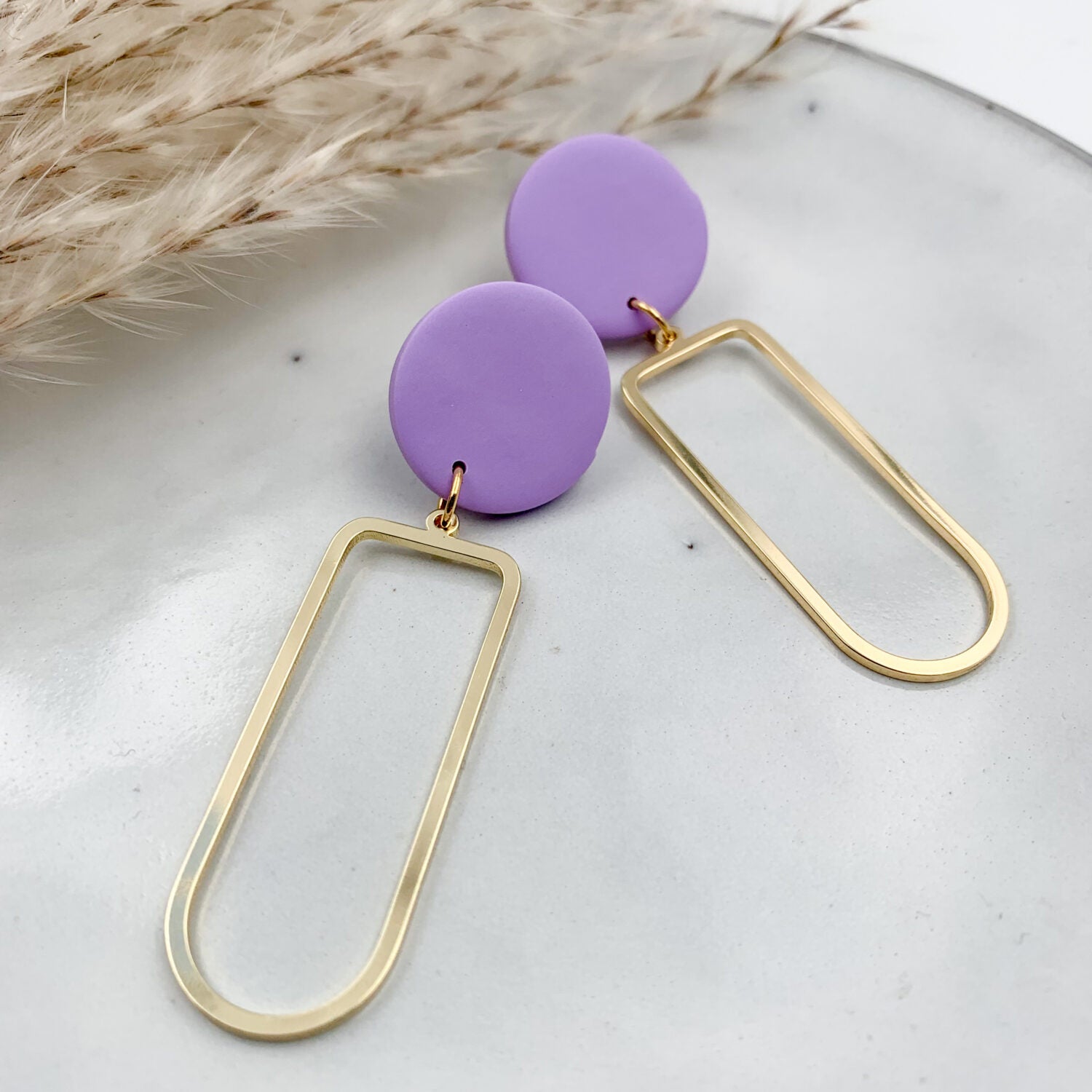 Lila Kreolen-Ohrringe mit goldenen rechteckigen Anhängern auf einem hellen Hintergrund.