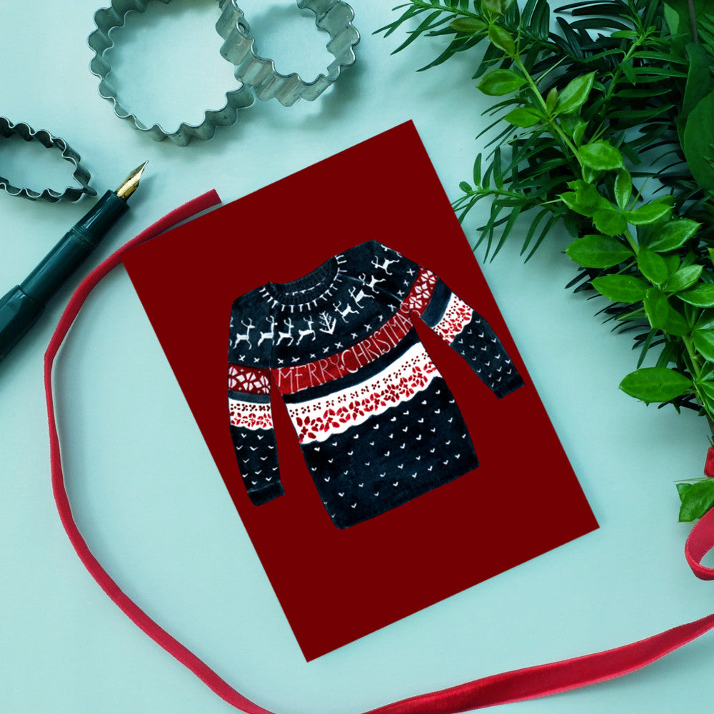 Christmas card with a dark blue sweater featuring a "Merry Christmas" design, surrounded by cookie cutters and greenery.