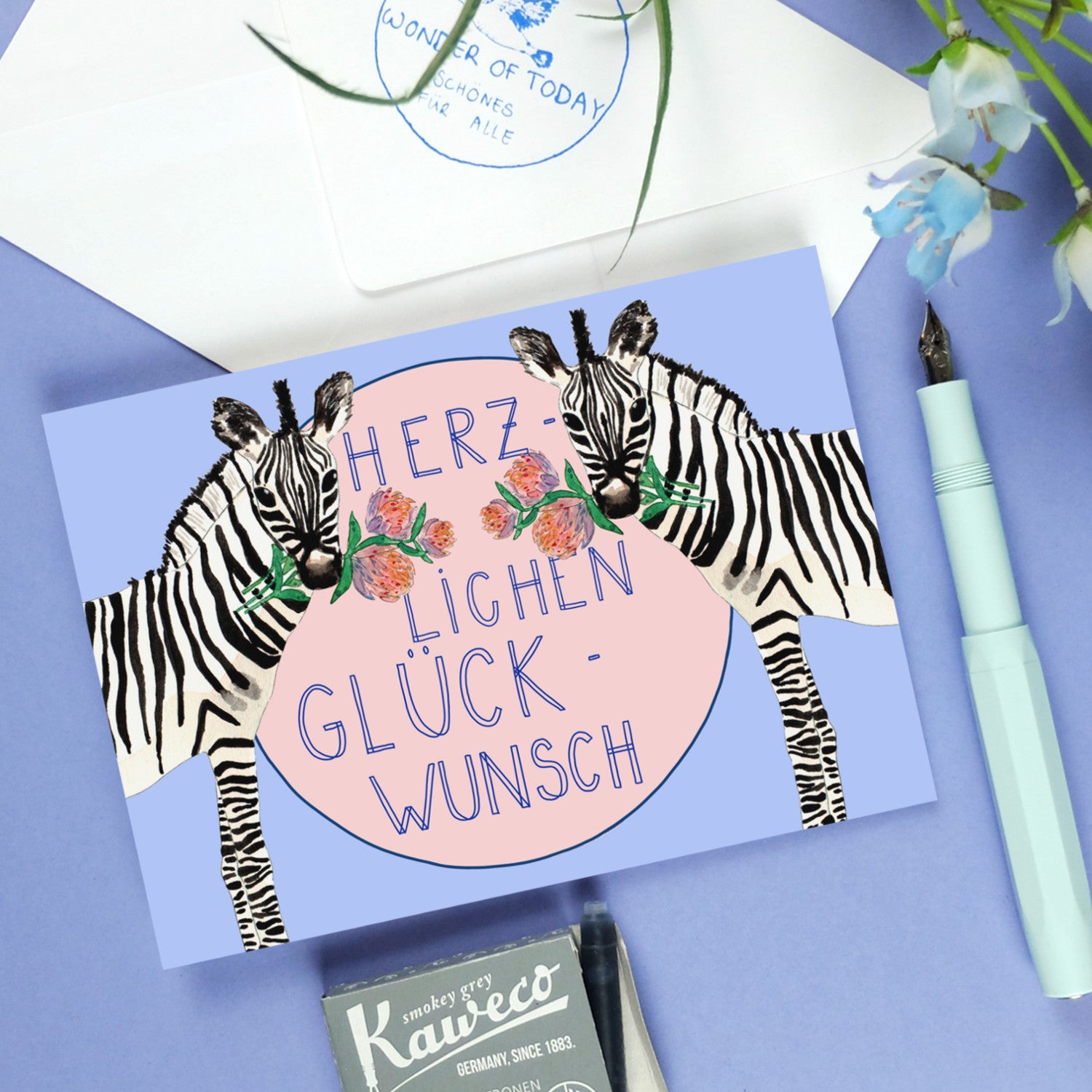Eine Glückwunschkarte mit Zebras, Blumen und dem Text "Herzlichen Glückwunsch" auf rosa Hintergrund.