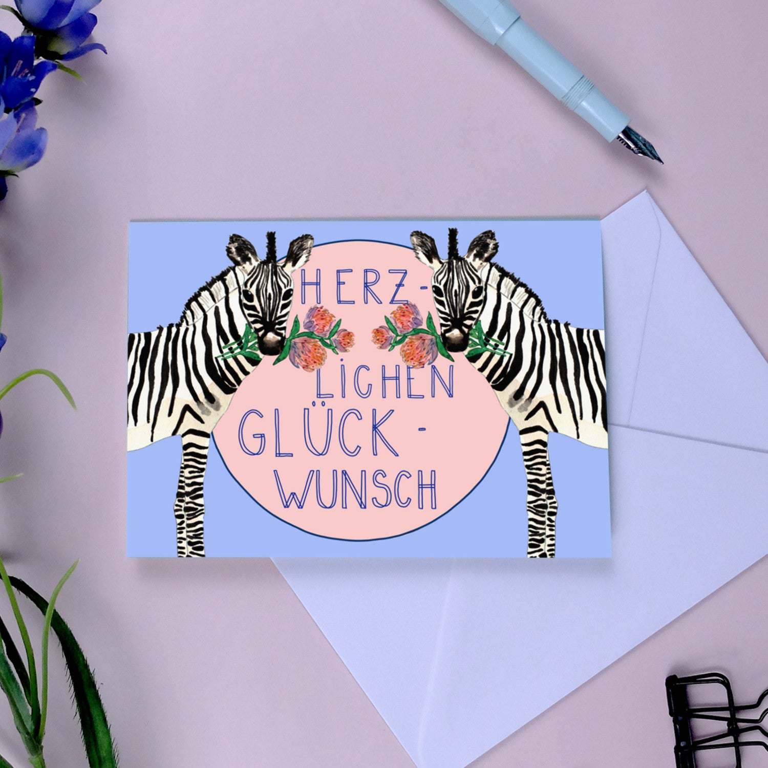 Karte mit Zebras, Blumen und dem Text "Herzlichen Glückwunsch" auf blauem und rosa Hintergrund.
