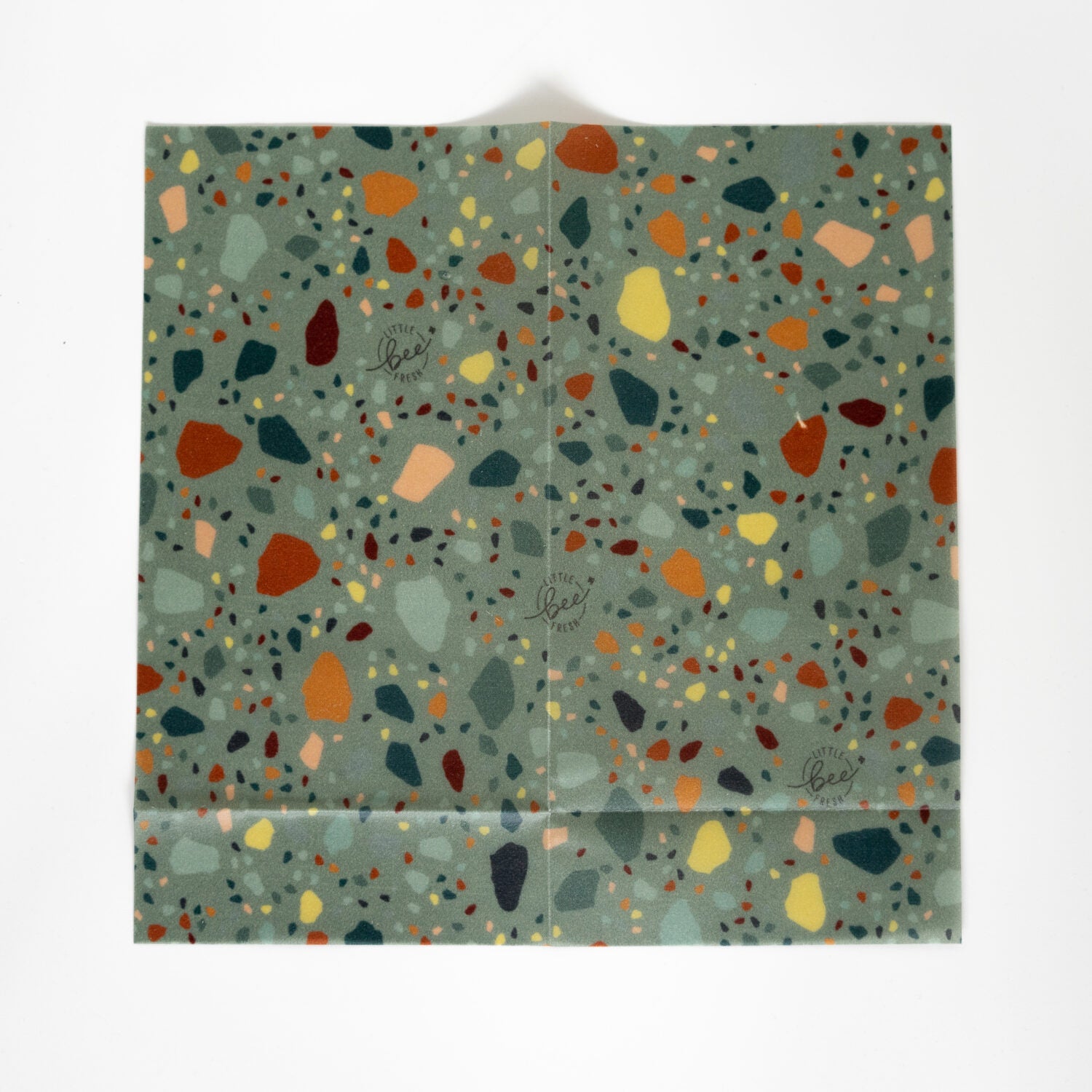 Grünes Wachstuch mit buntem Terrazzo-Muster und kleinen Logos in der Mitte.