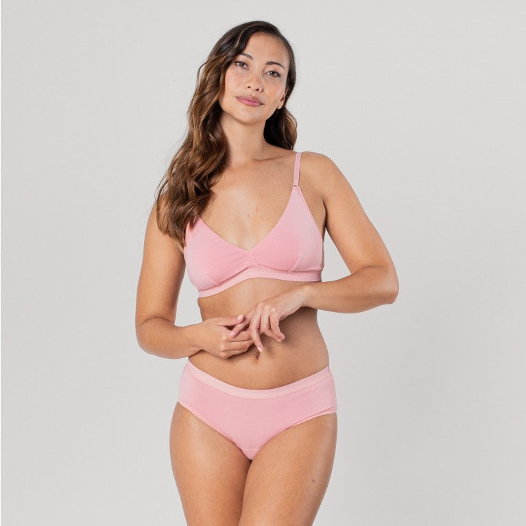 Frau in rosa Unterwäsche vor neutralem Hintergrund.