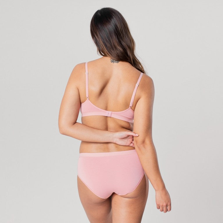 Eine Frau in rosa Unterwäsche steht mit dem Rücken zur Kamera und neigt den Kopf leicht zur Seite.