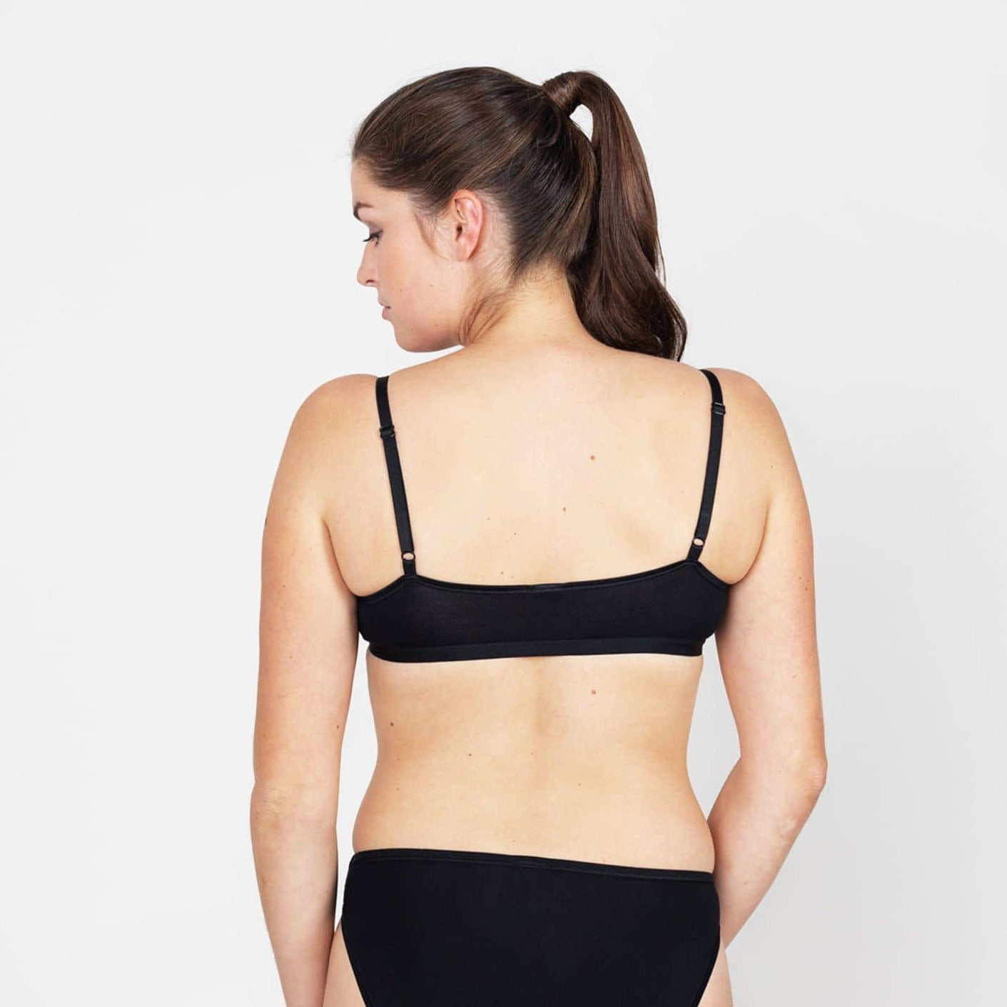 Frau von hinten in schwarzer Unterwäsche vor weißem Hintergrund.