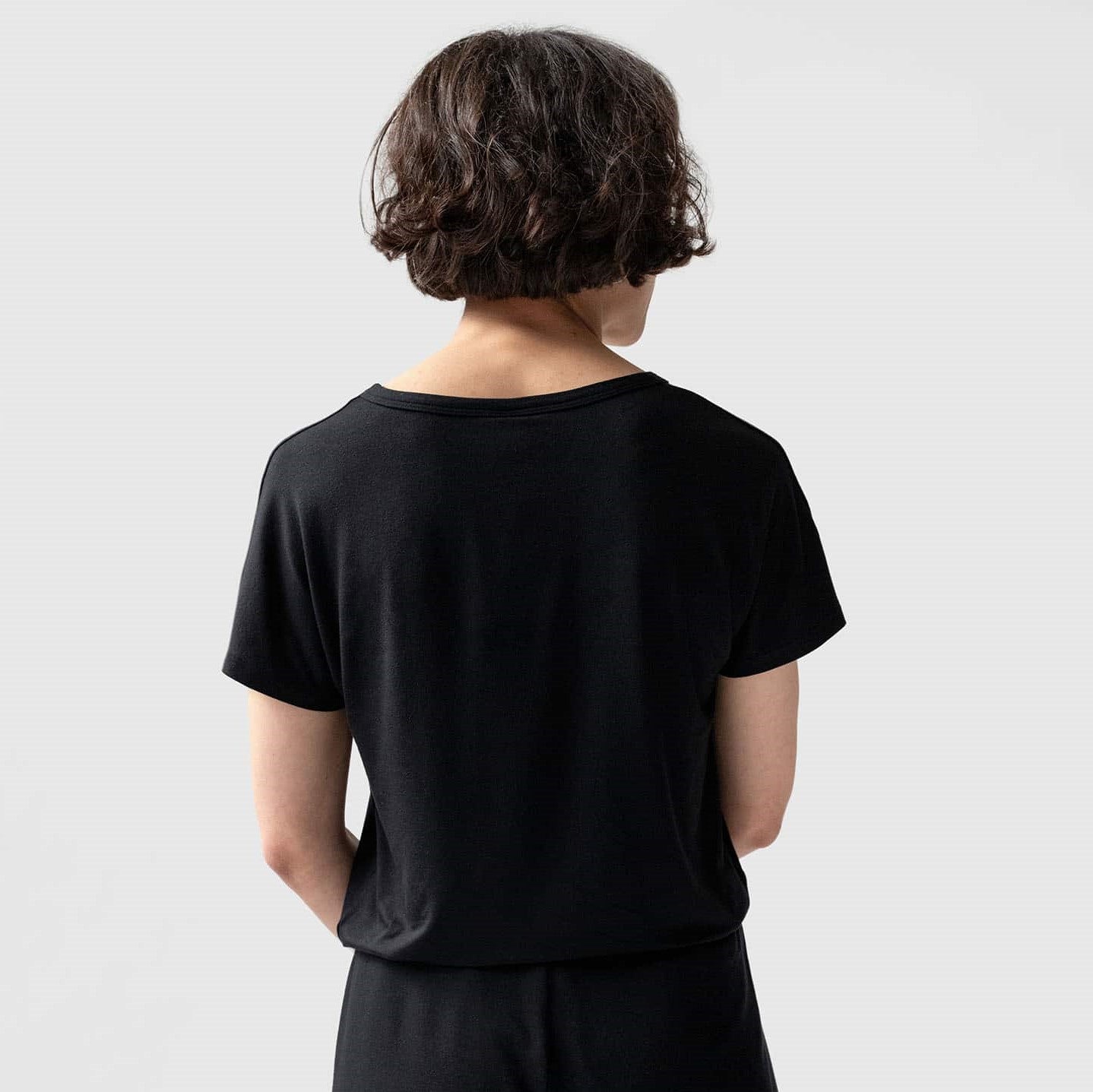 Eine Person mit braunen, lockigen Haaren trägt ein schwarzes T-Shirt und steht mit dem Rücken zur Kamera.