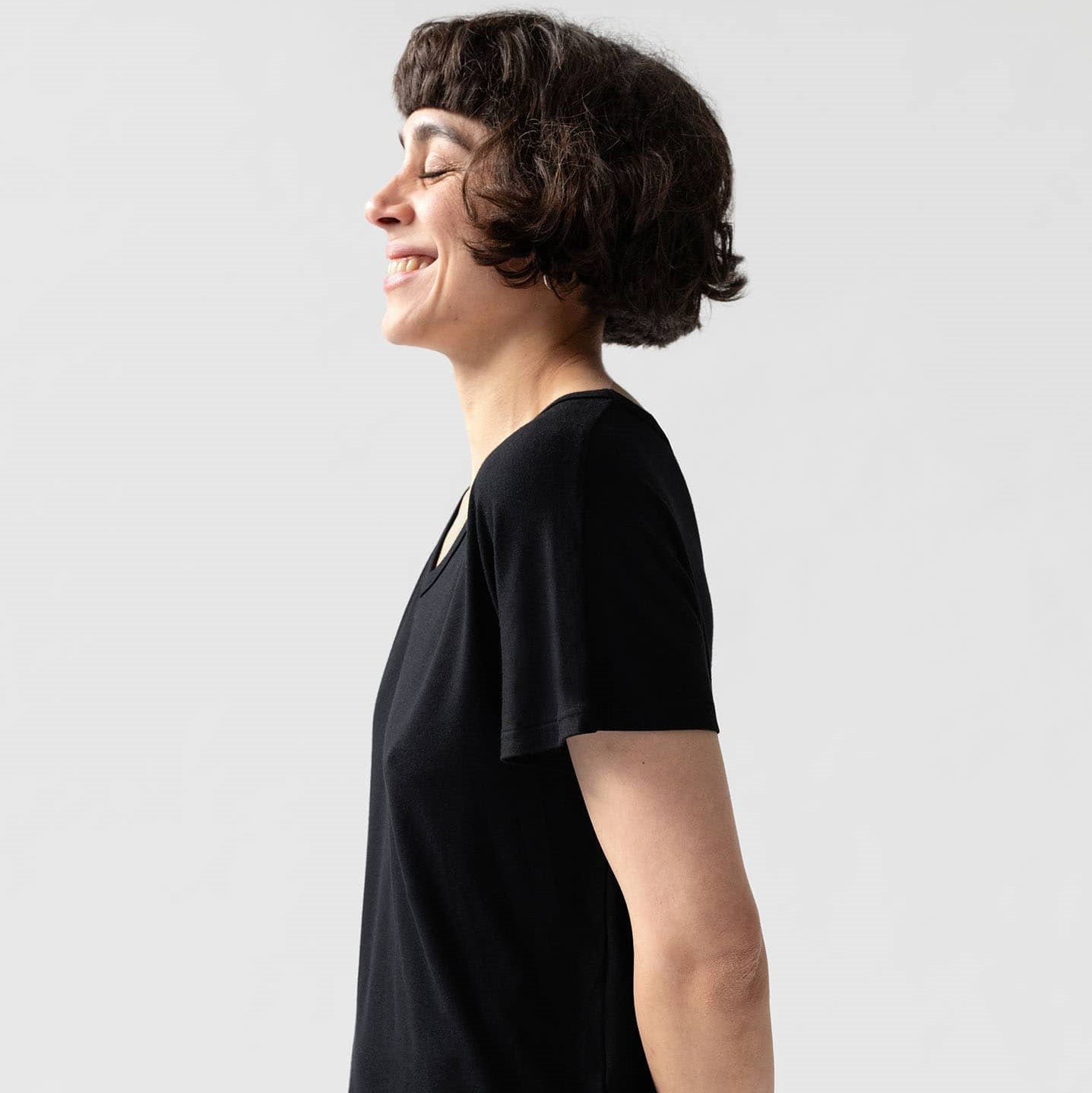Frau mit kurzen Haaren und schwarzem T-Shirt lächelt im Profil vor hellem Hintergrund.