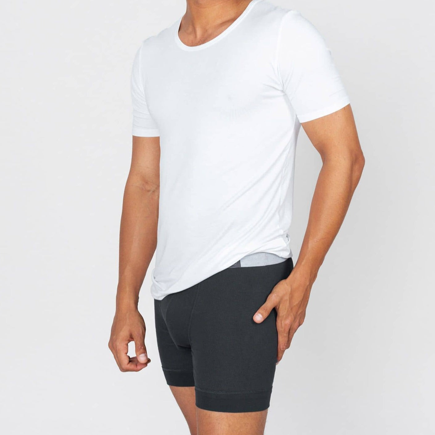 Mann trägt ein weißes T-Shirt und schwarze Boxershorts vor neutralem Hintergrund.