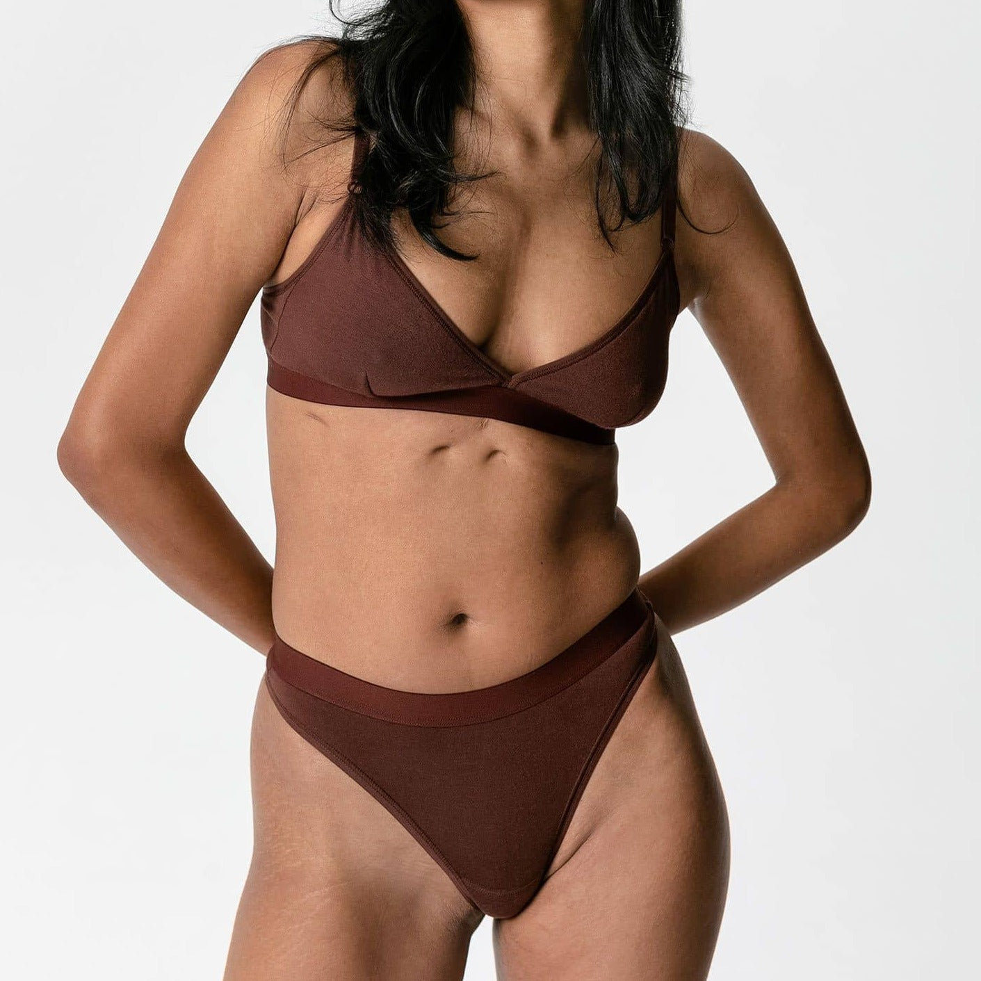 Eine Frau trägt braune Unterwäsche und steht vor einem weißen Hintergrund.