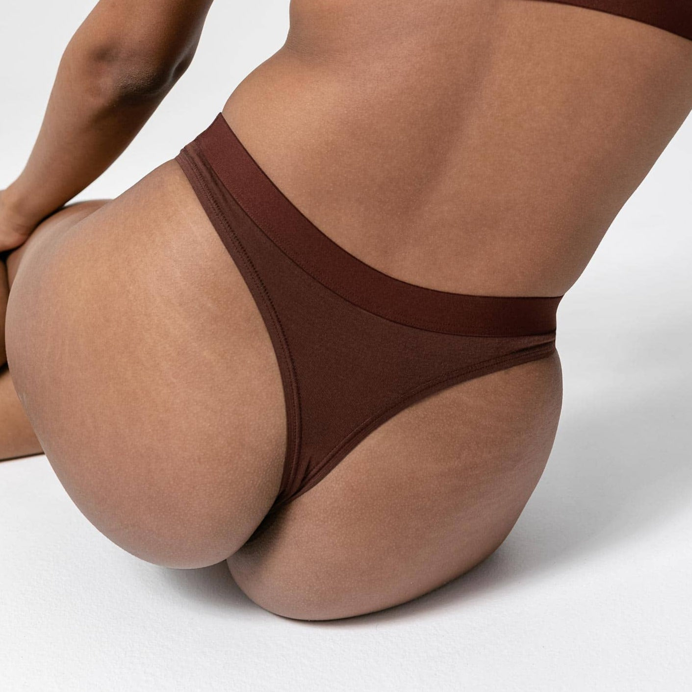 Person in brown underwear sitting on a white surface, focusing on their lower back and hips.