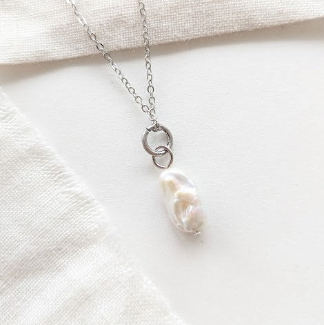 Silberne Halskette mit einer weißen Perlenanhänger auf einem weißen Tuchhintergrund.