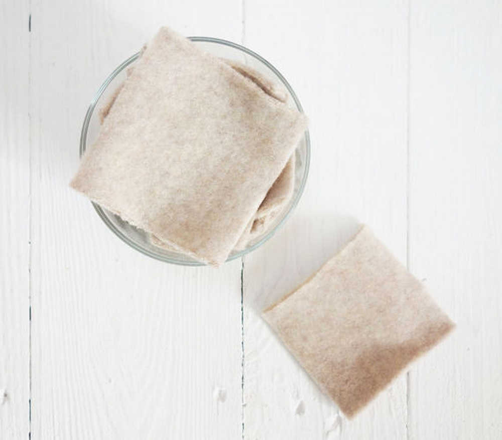 Ein Glasbehälter mit quadratischen Stofftüchern auf einem weißen Holztisch, eins liegt daneben.