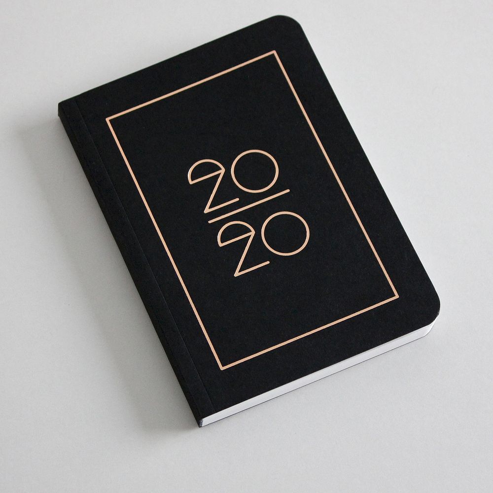 Schwarzes Notizbuch mit der Aufschrift "20/20" in einem goldenen Rahmen auf dem Cover.