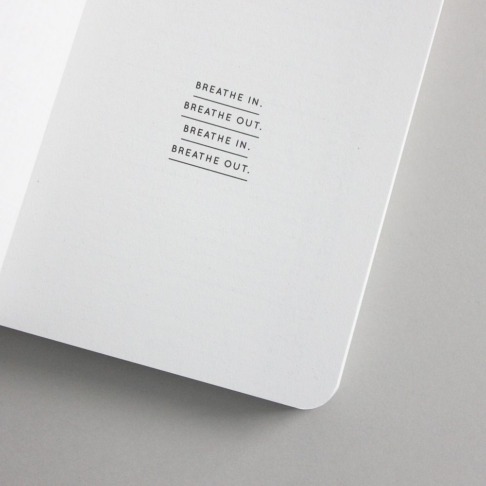 Weiße Buchseite mit dem Text "BREATHE IN. BREATHE OUT. BREATHE IN. BREATHE OUT." in schwarzer Schrift.