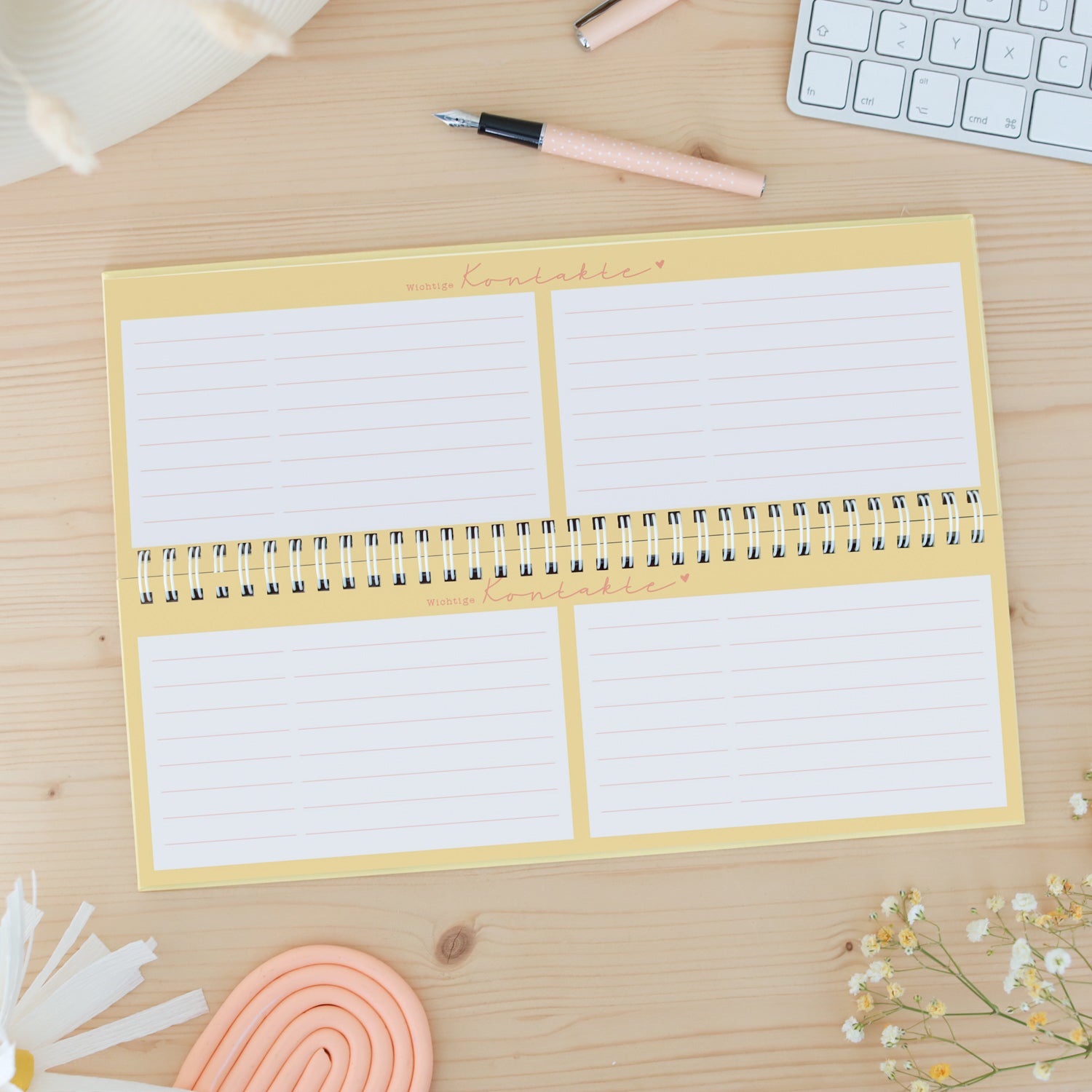 Gelbes Kontaktbuch auf einem Schreibtisch mit Stift, Tastatur und Blumen.